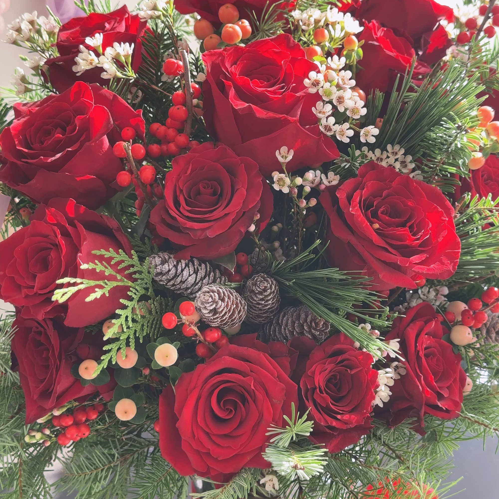 Red roses arranged with pine, berries, and pinecones in a vase