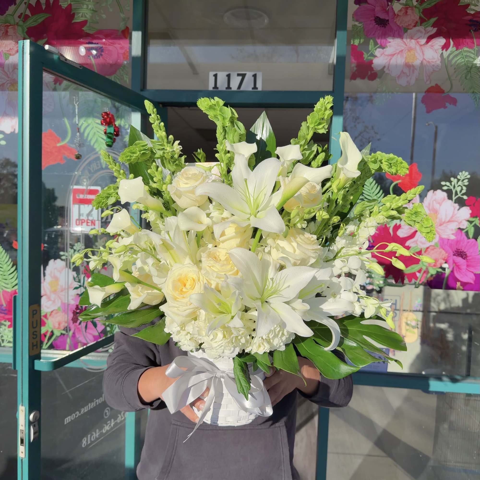 White lilies and roses arranged in a white basket with a silver ribbon