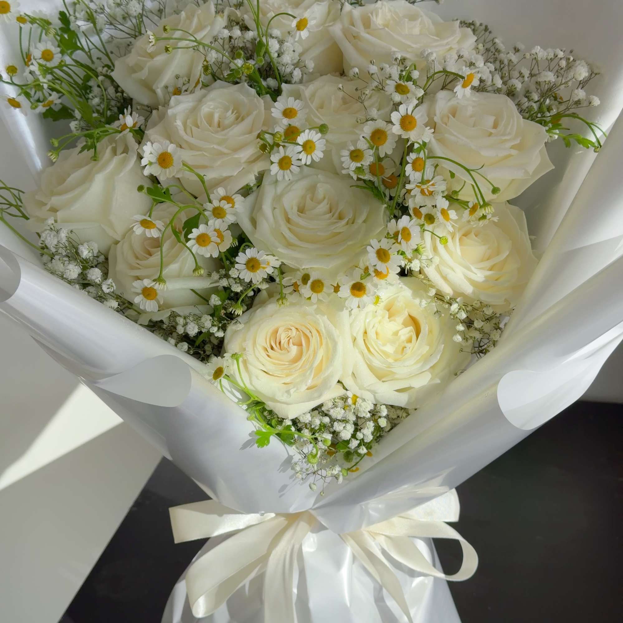 Bouquet of white roses and small white daisies wrapped in white paper