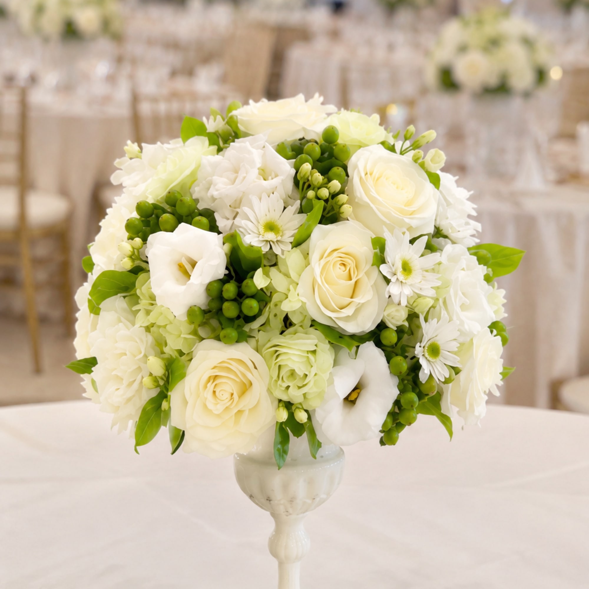 White floral arrangement in a pedestal vase with green accents