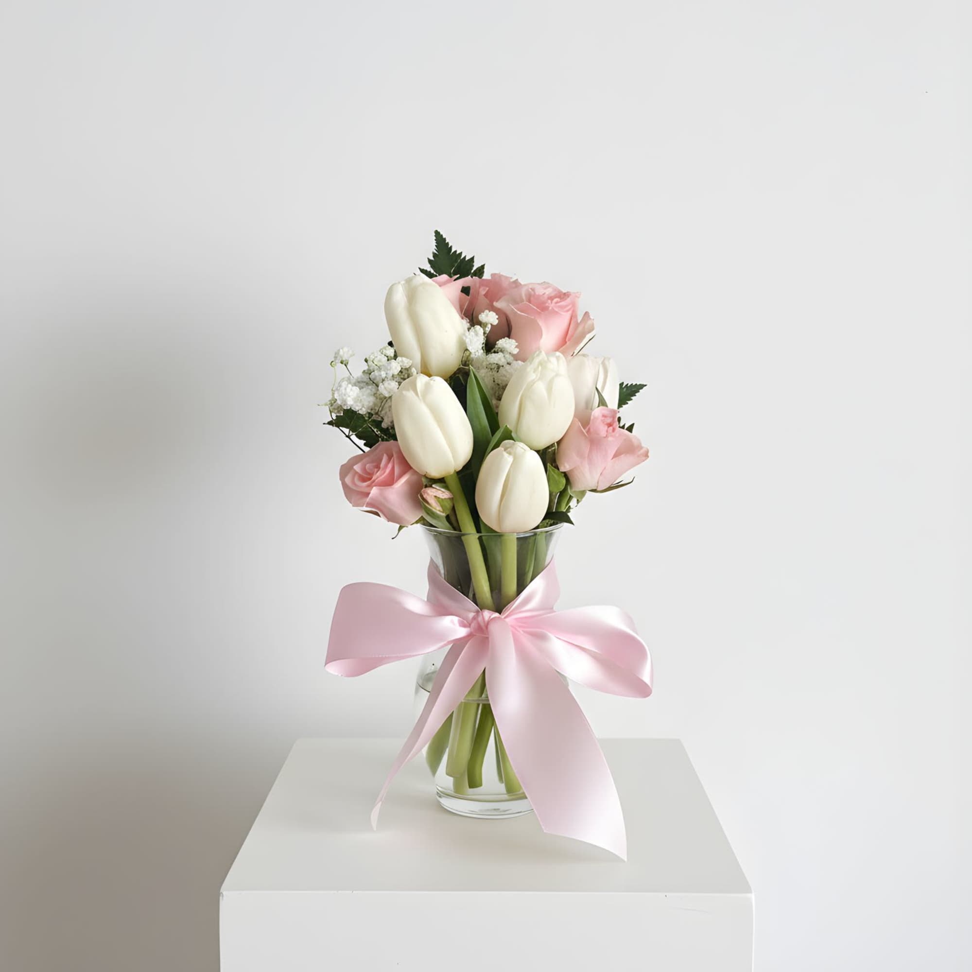 Pink roses and white tulips in a glass vase with a pink ribbon