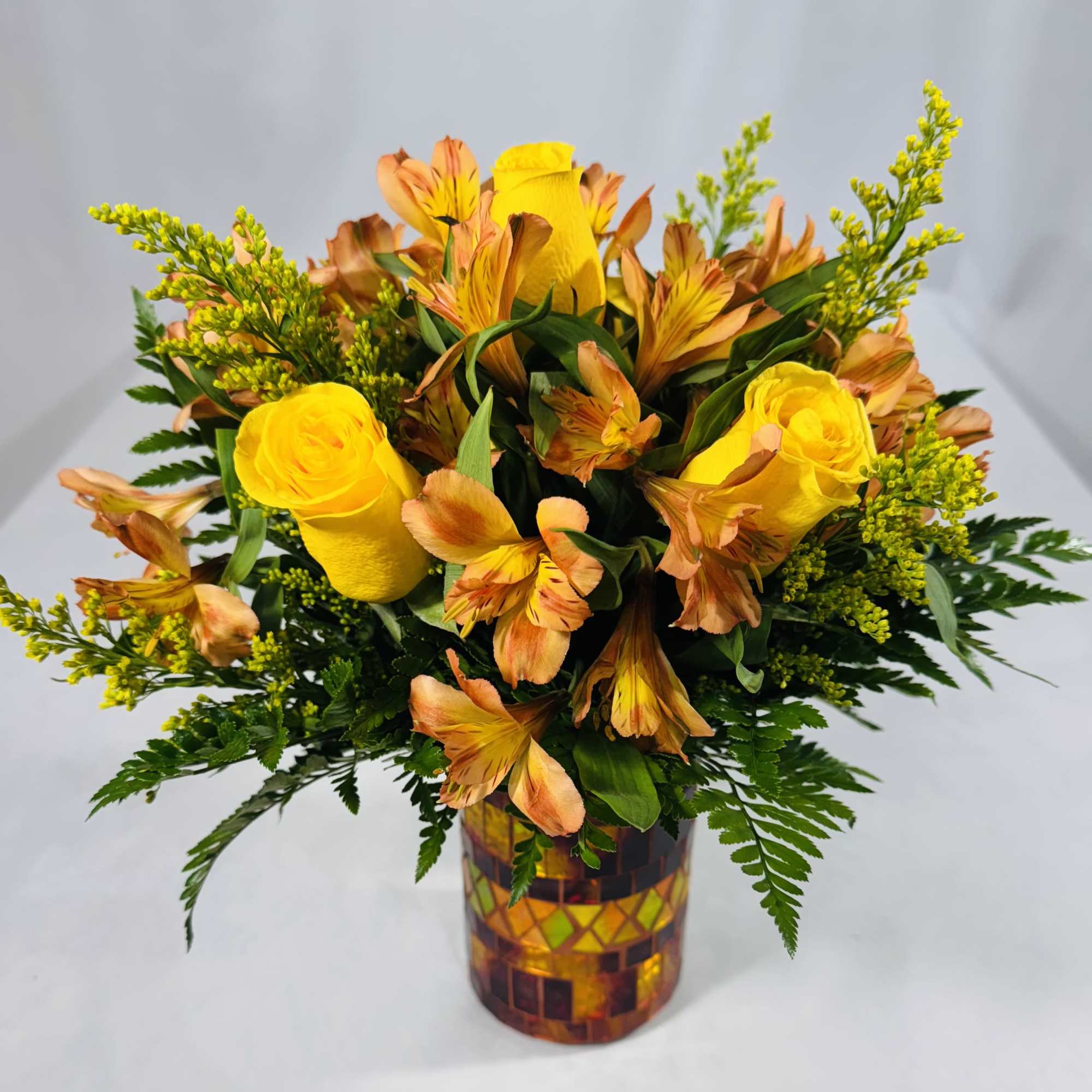 Yellow roses and orange alstroemeria in a mosaic glass vase.