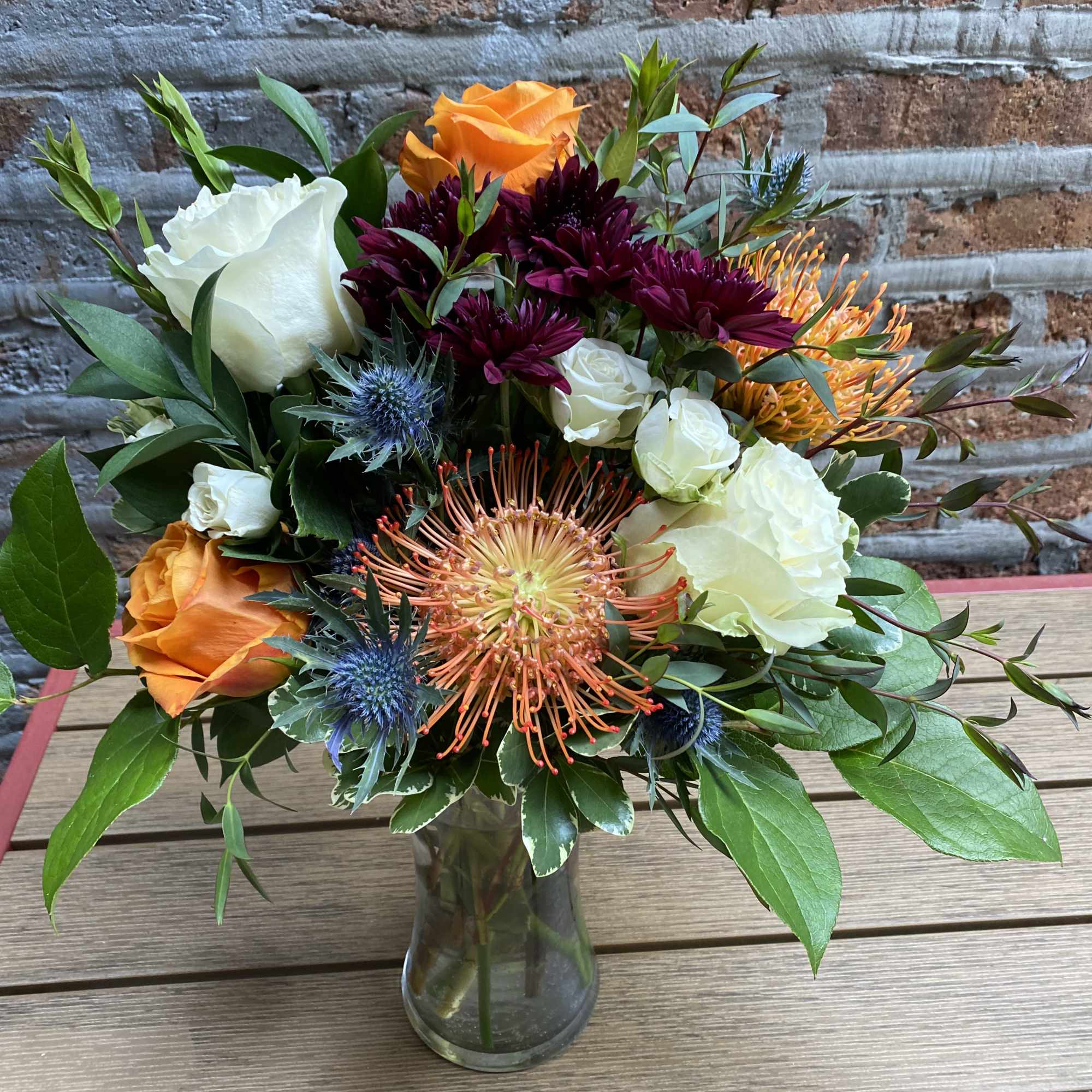 Mixed bouquet of orange, white, and burgundy flowers in a glass vase