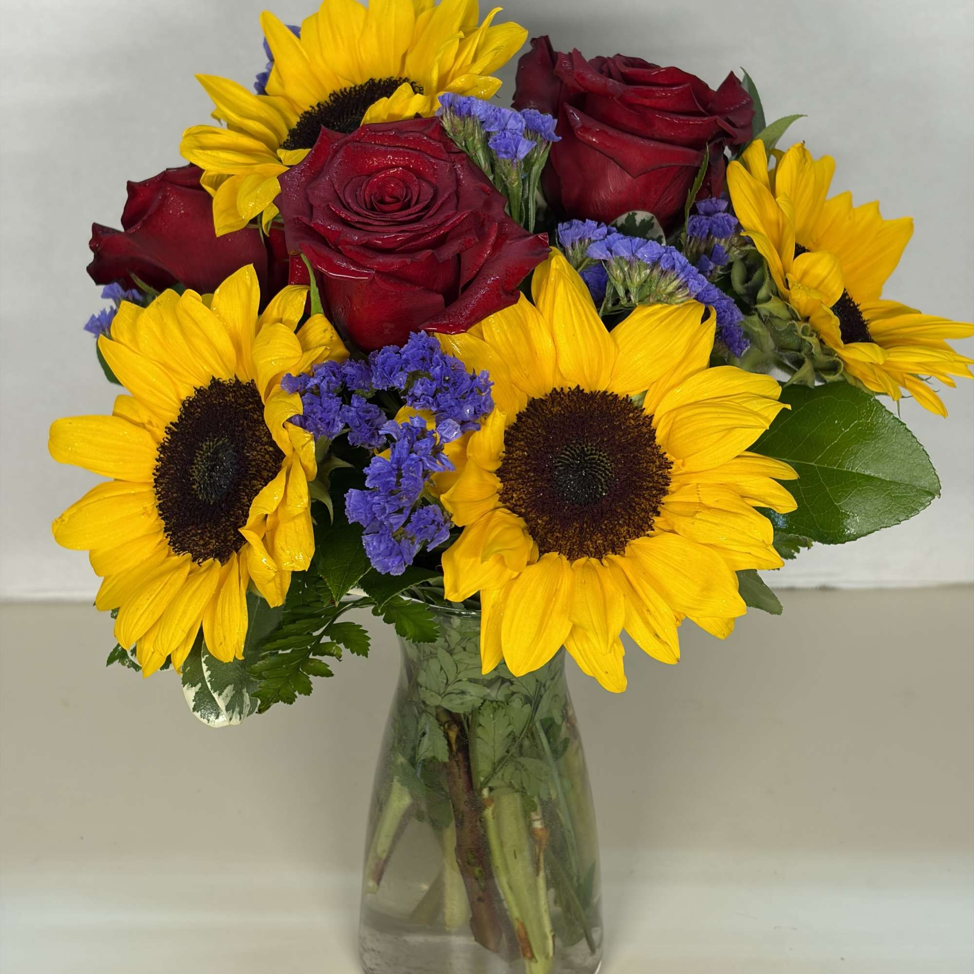 Bouquet of red roses and yellow sunflowers in a clear glass vase