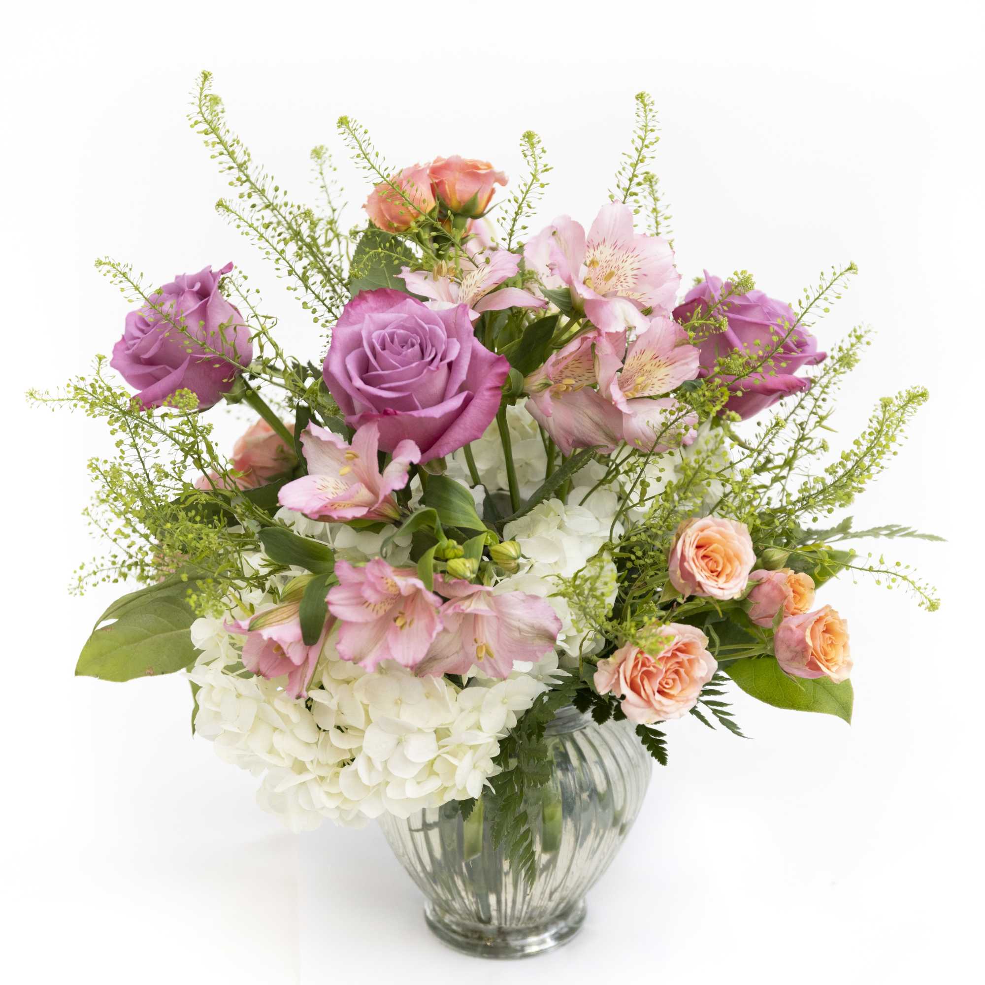 Mixed bouquet of lavender roses, peach spray roses, pink alstroemeria, and white hydrangeas in a glass vase