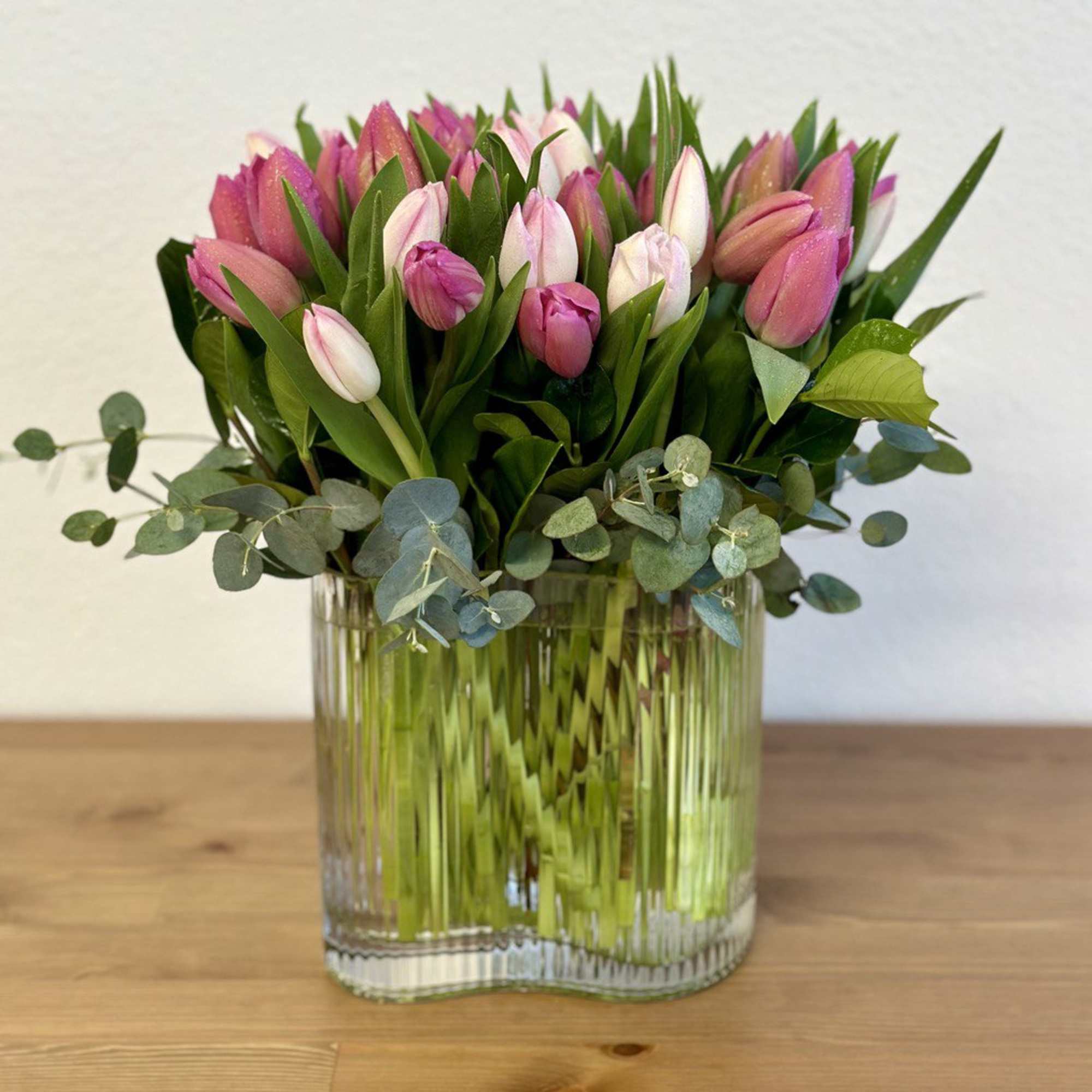 Pink tulips arranged in a clear glass vase with eucalyptus