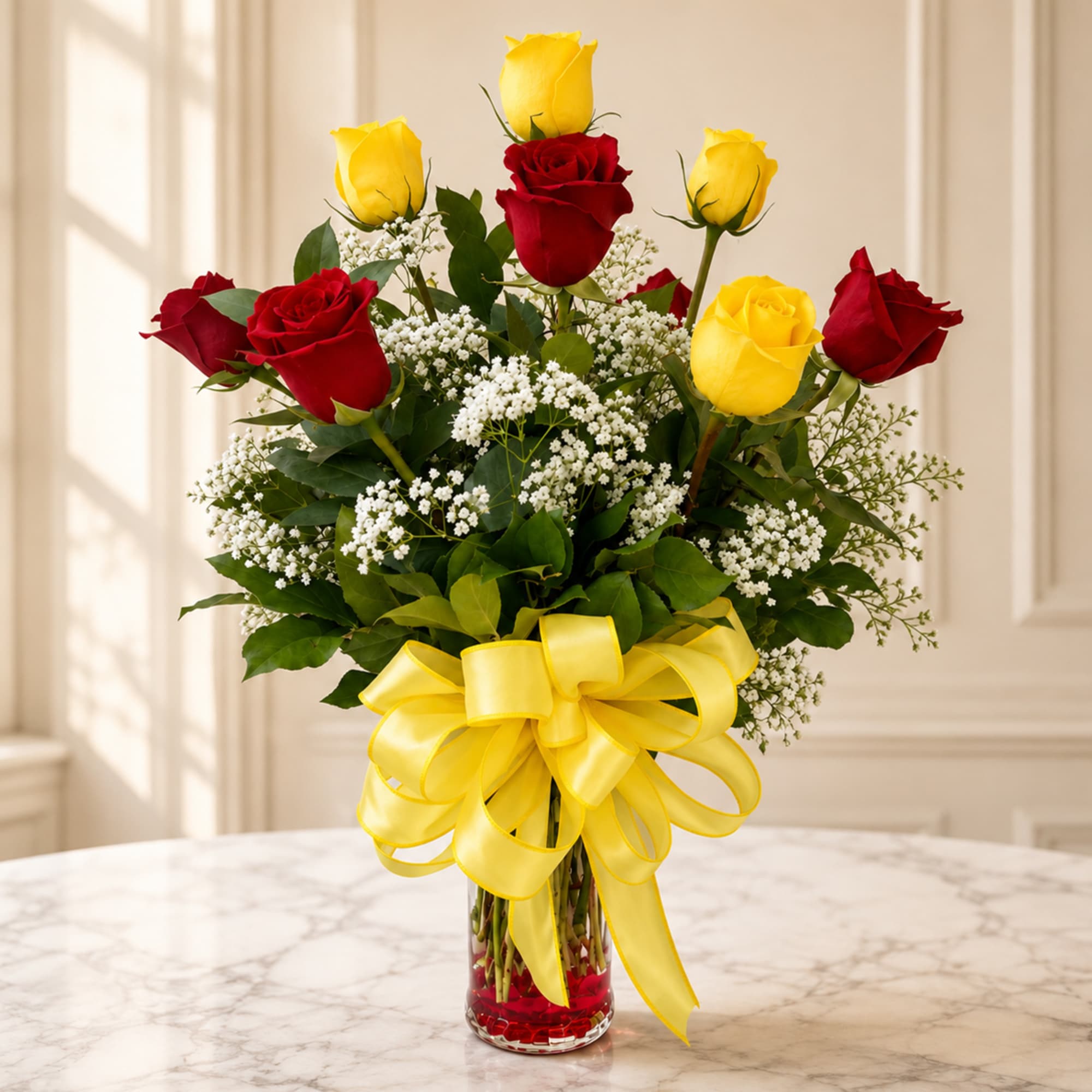 Bouquet of red and yellow roses in a clear glass vase with a yellow ribbon