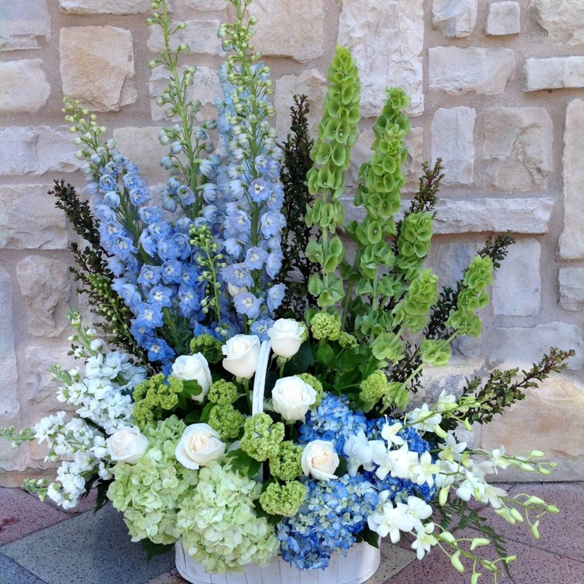 Large blue, white, and green floral arrangement in a white basket
