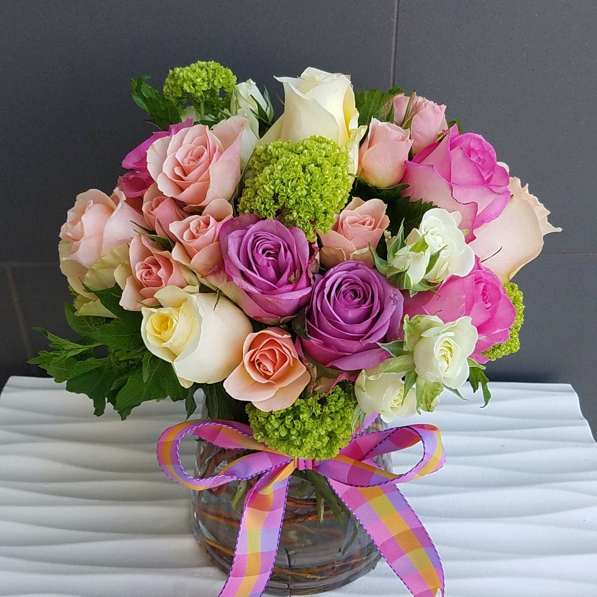 Bouquet of pink, purple, white, and peach roses in a glass vase with a ribbon bow