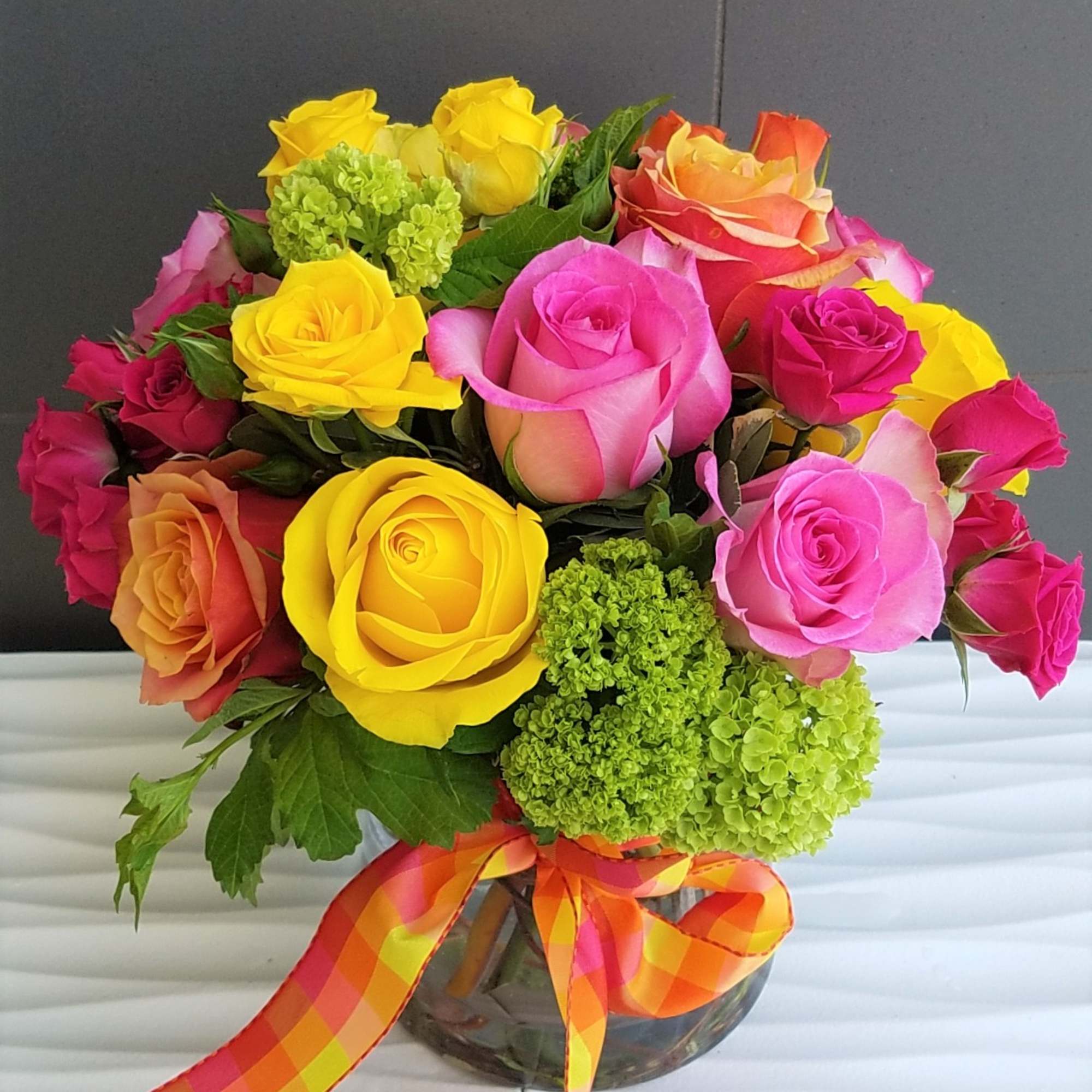 Colorful bouquet of roses in a glass vase with a plaid ribbon