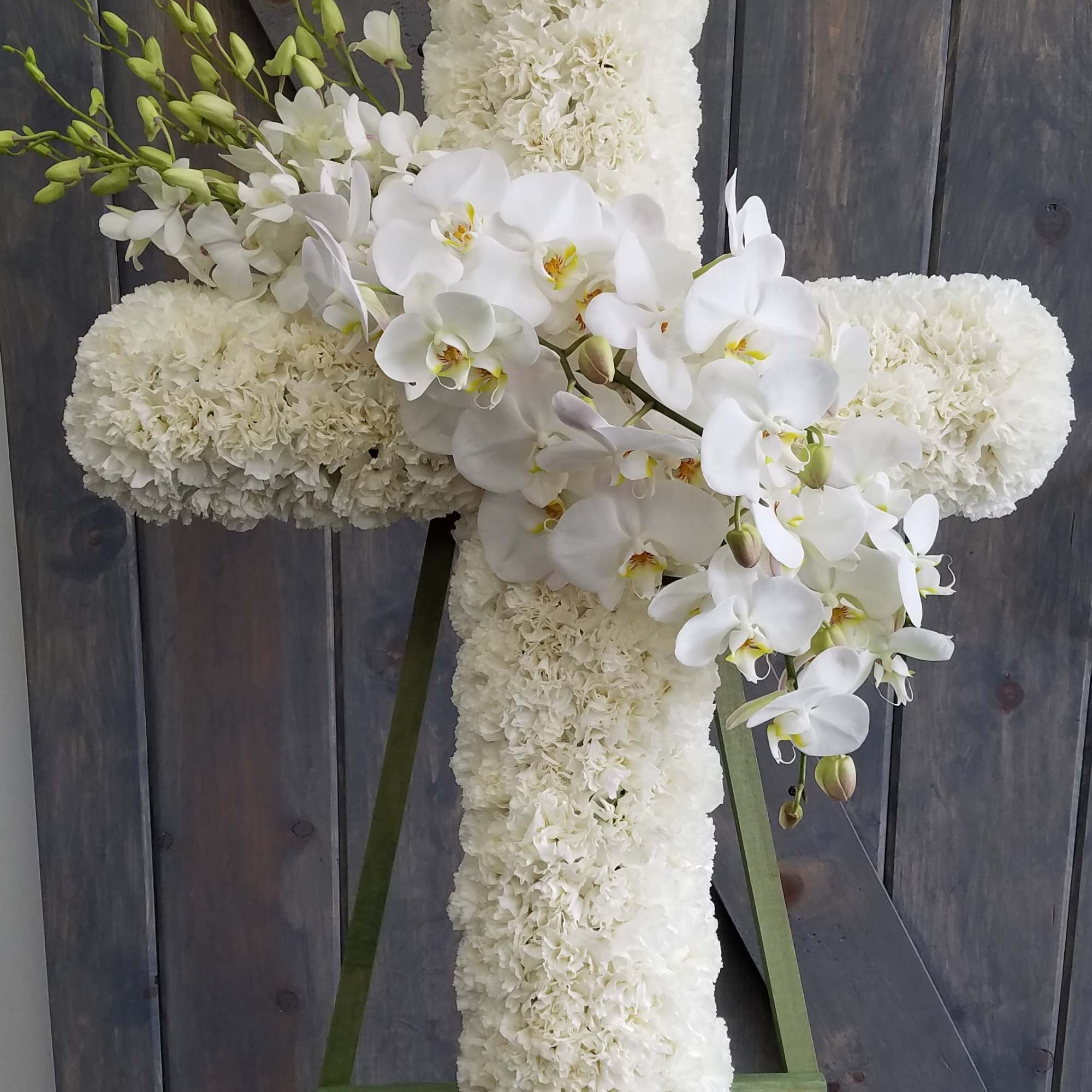 White floral cross on an easel with orchids and carnations