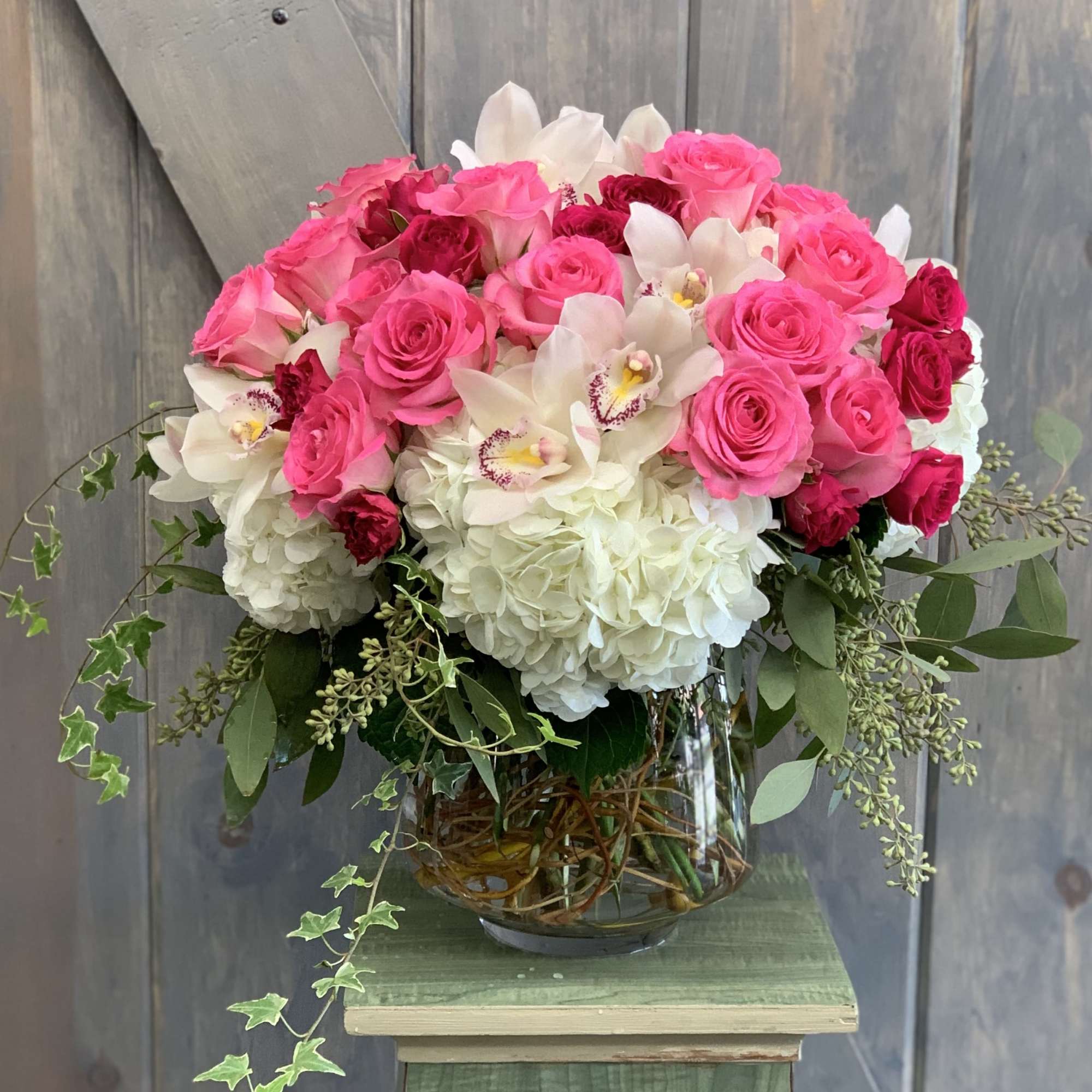 Pink roses and white hydrangeas in a glass vase with trailing greenery