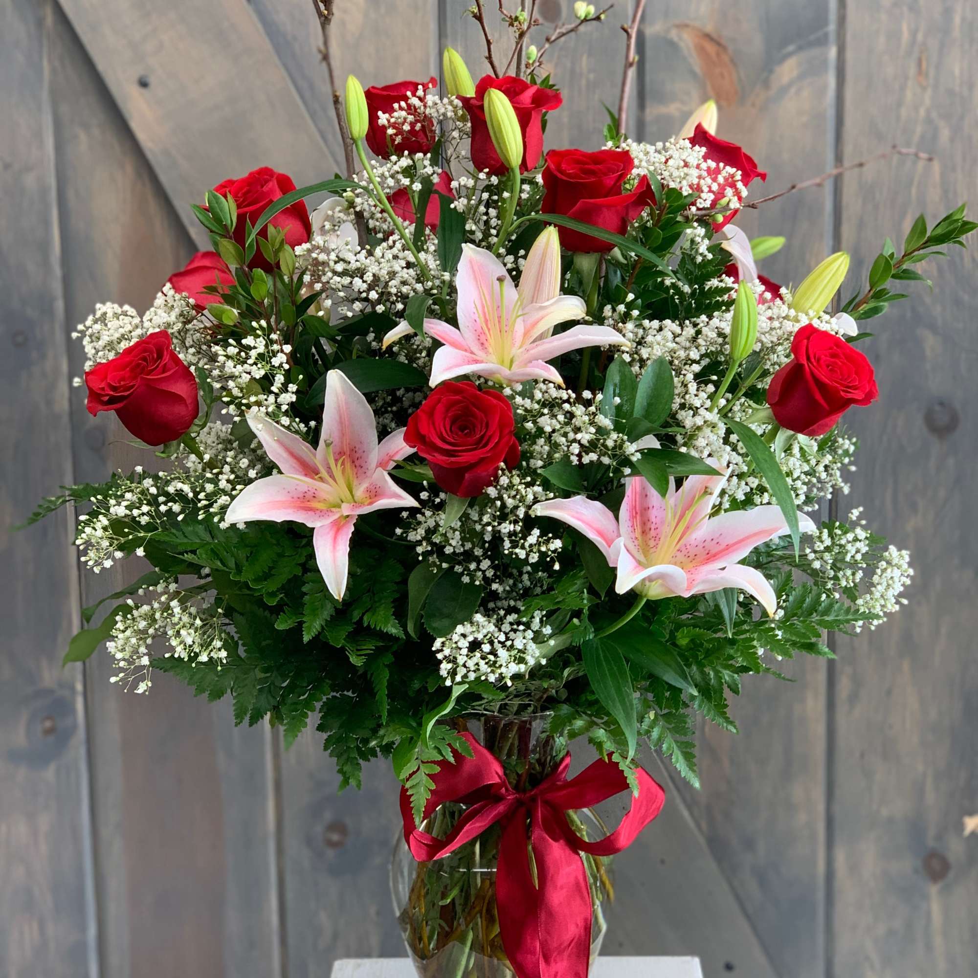 Red roses and pink lilies in a glass vase with a red ribbon
