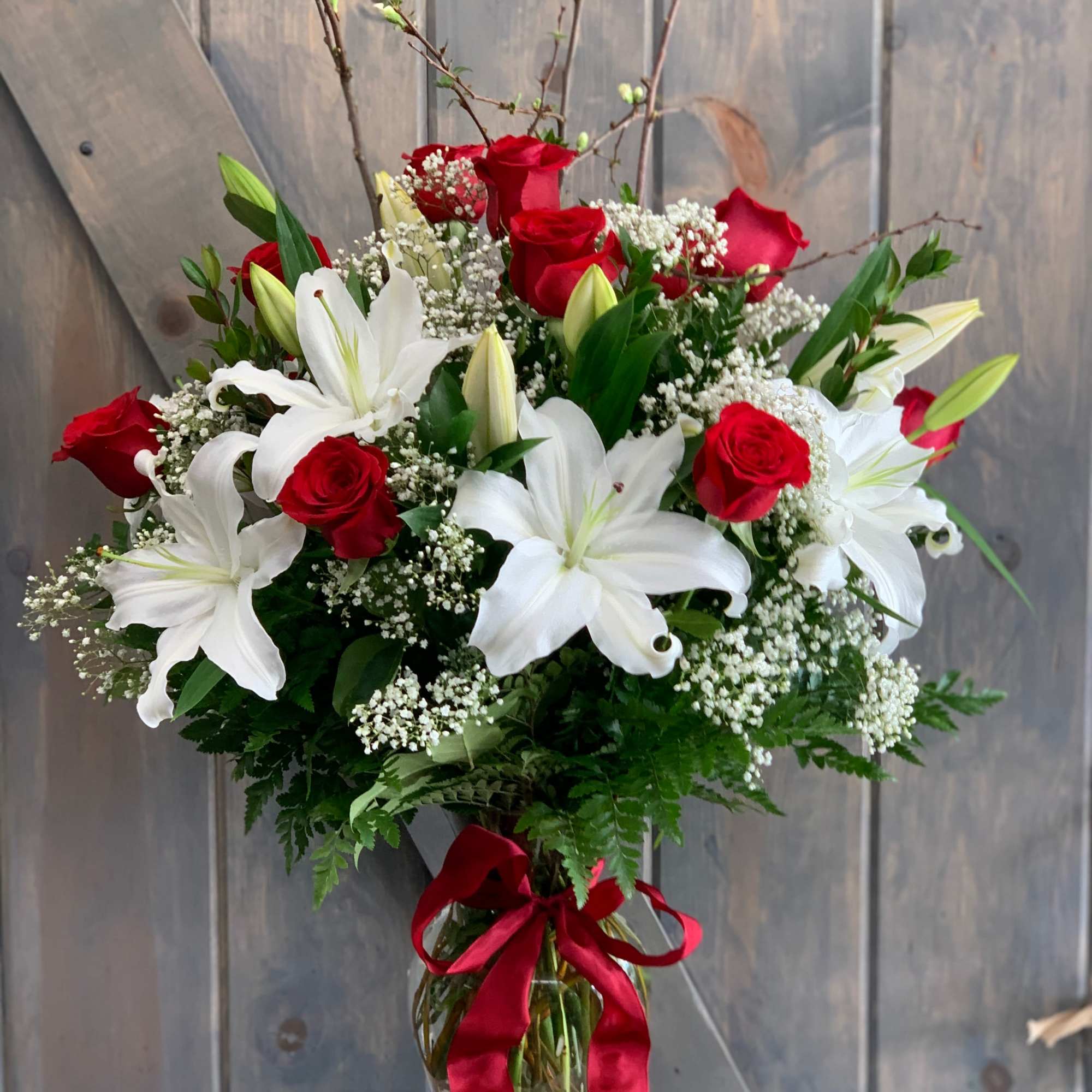 Bouquet of red roses and white lilies in a glass vase with a red ribbon