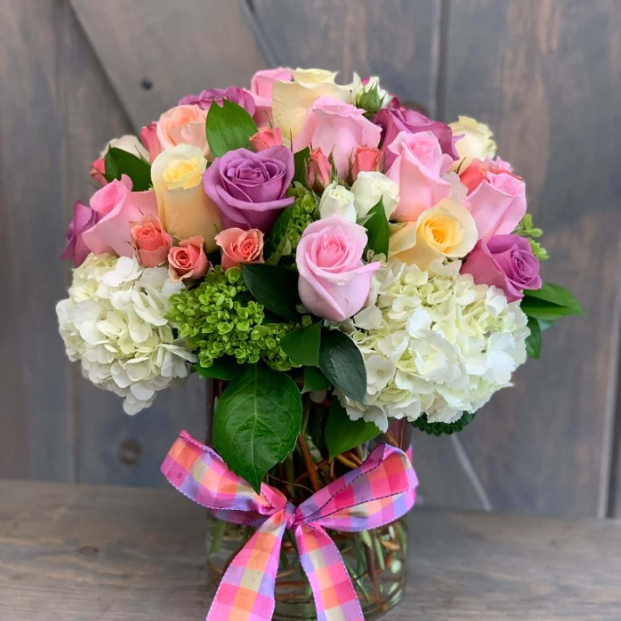Bouquet of pink, purple, and white roses in a glass vase with a plaid ribbon