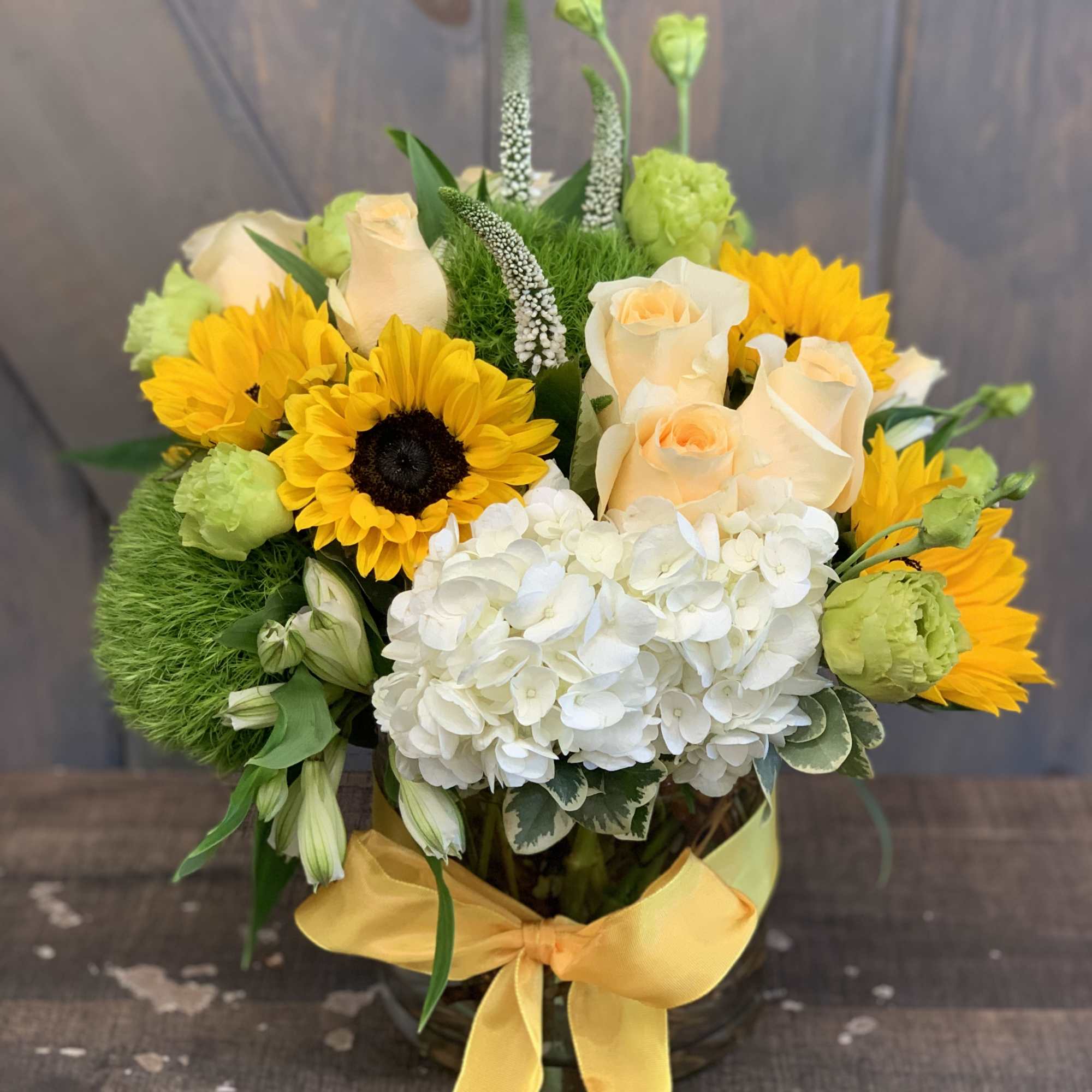 Bouquet of yellow sunflowers, cream roses, and white hydrangea in a glass vase