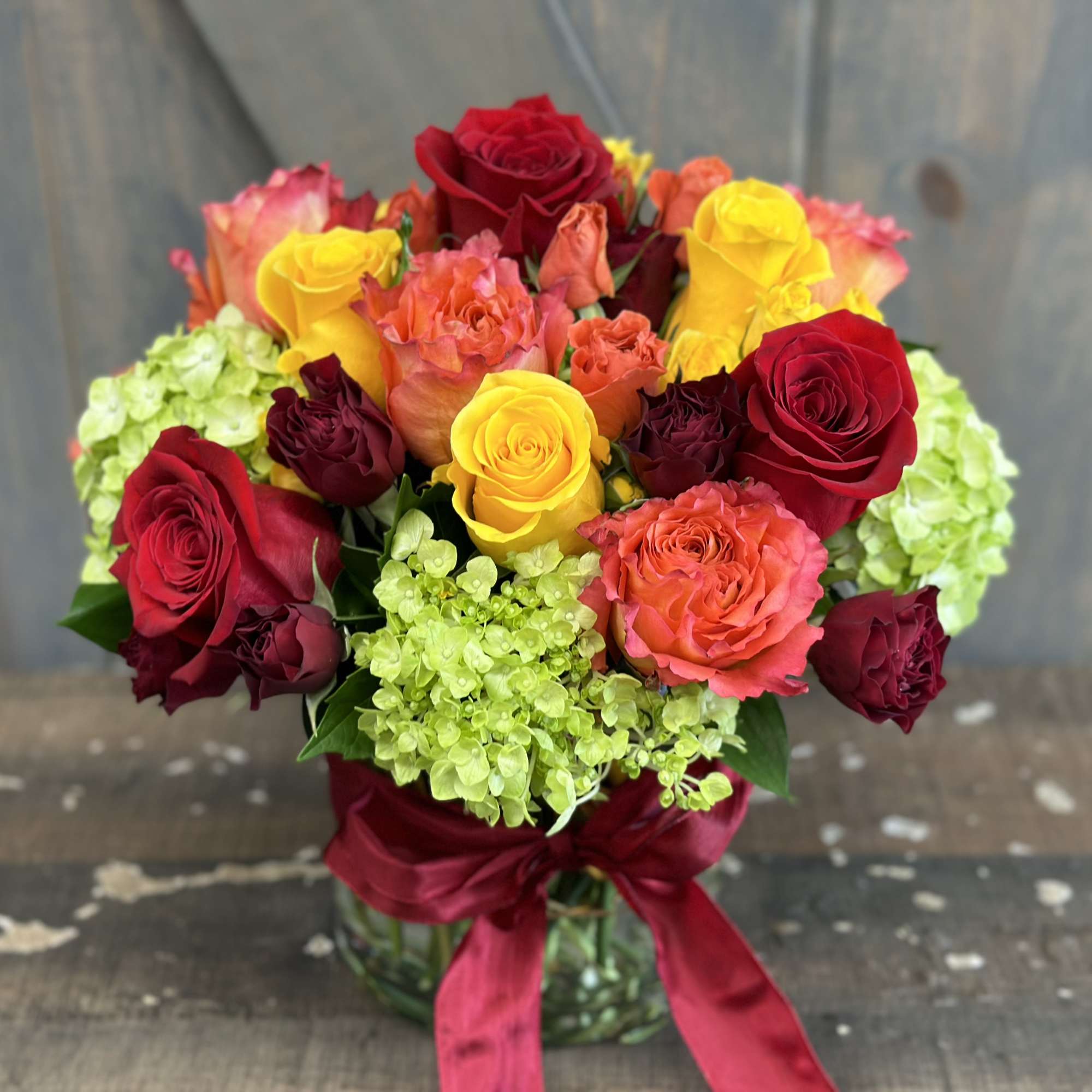 Bouquet of red, yellow, and coral roses in a glass vase with a red ribbon
