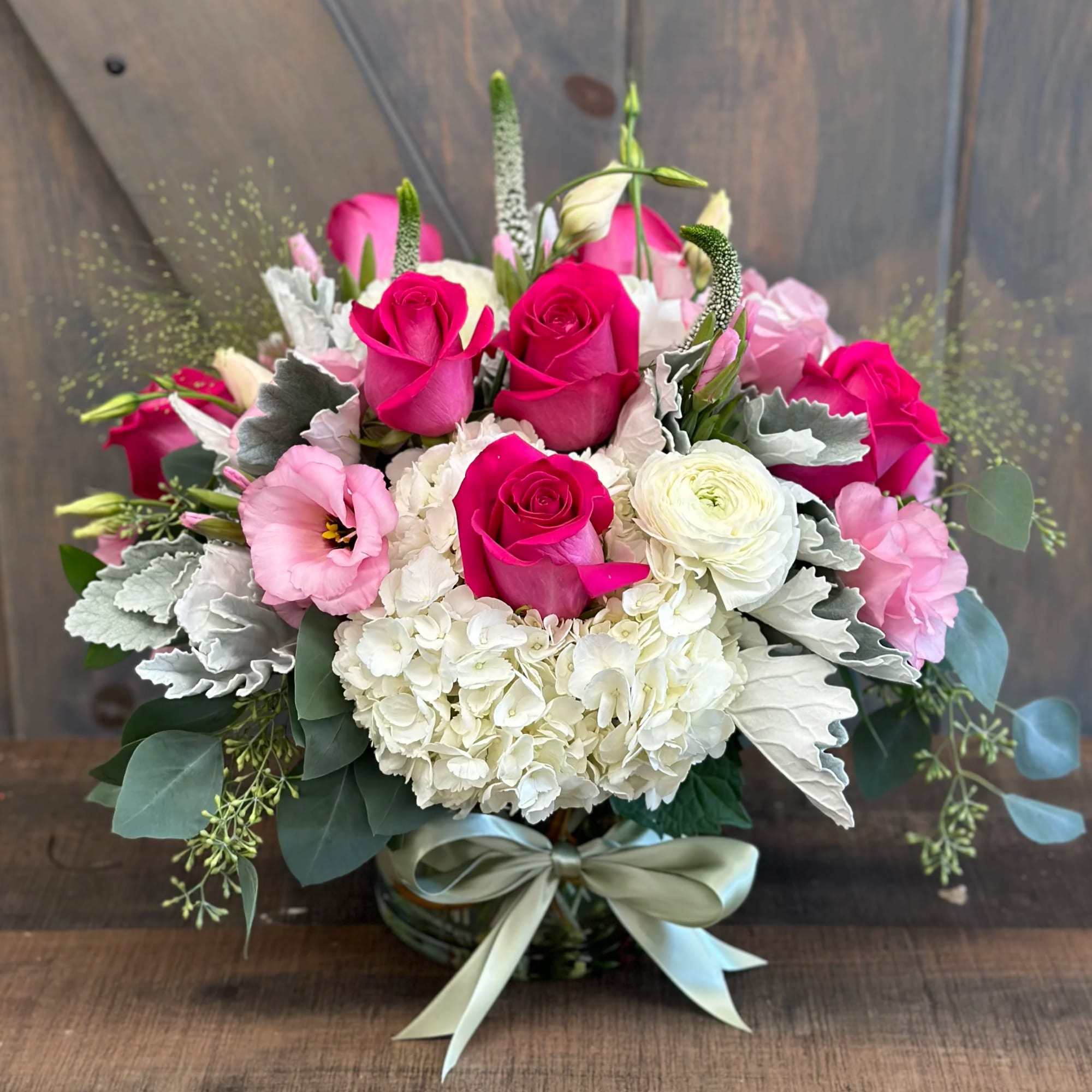 Pink roses and white blooms arranged in a glass vase with a ribbon