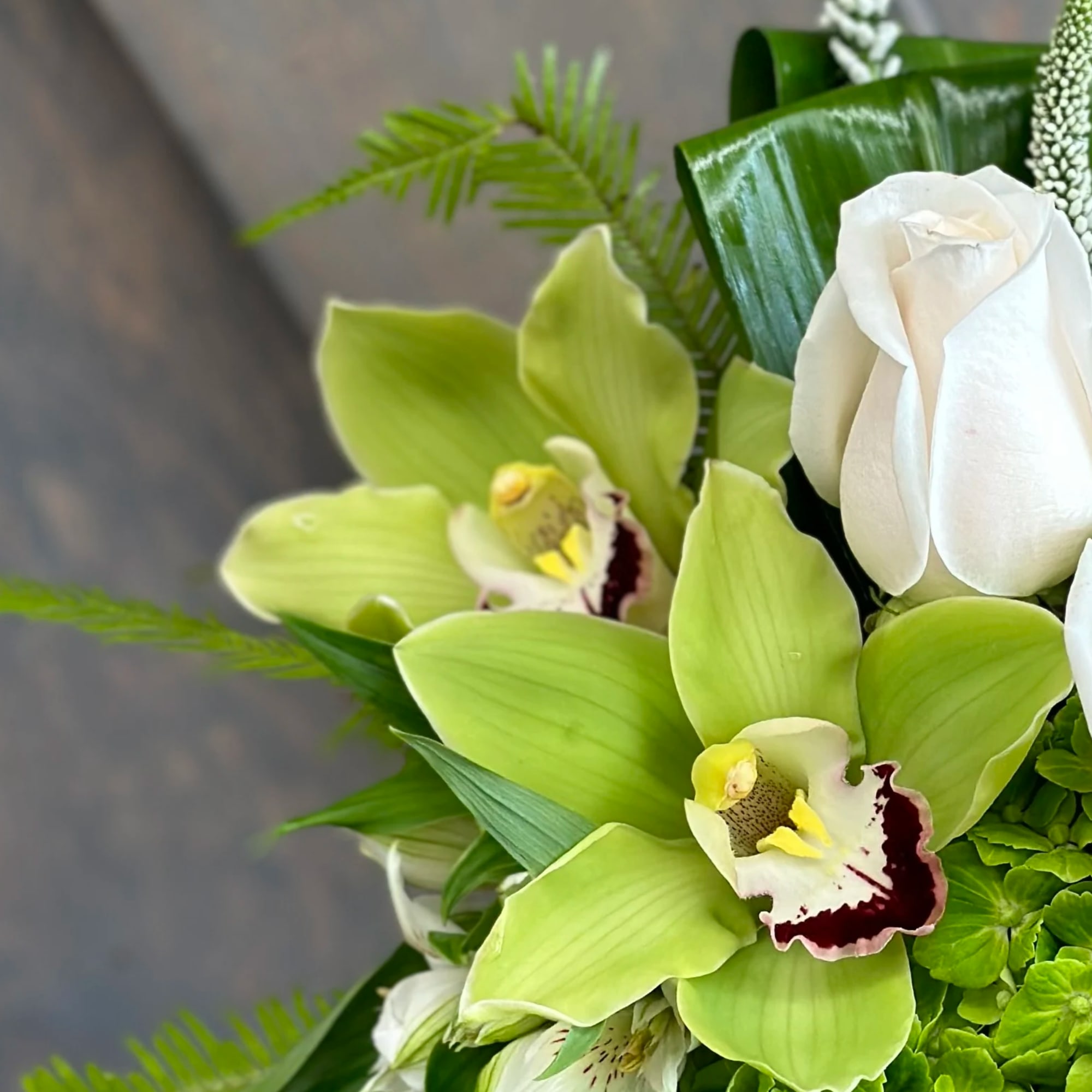 Green and white floral arrangement with orchids and a white rose