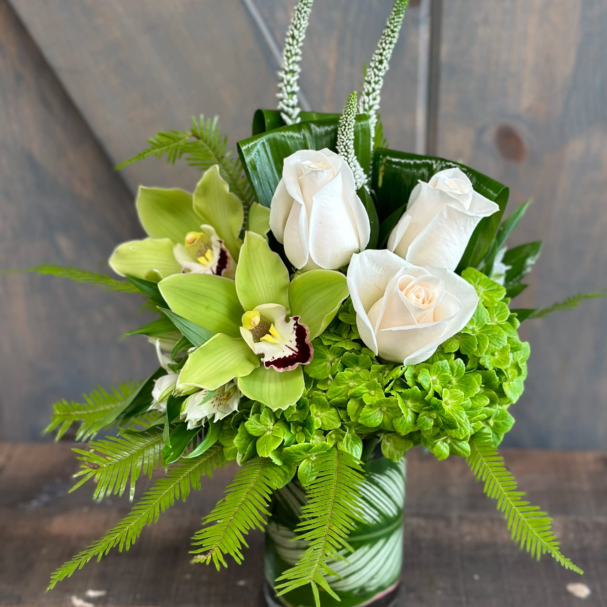 White roses and green orchids in a glass vase with bright green hydrangea