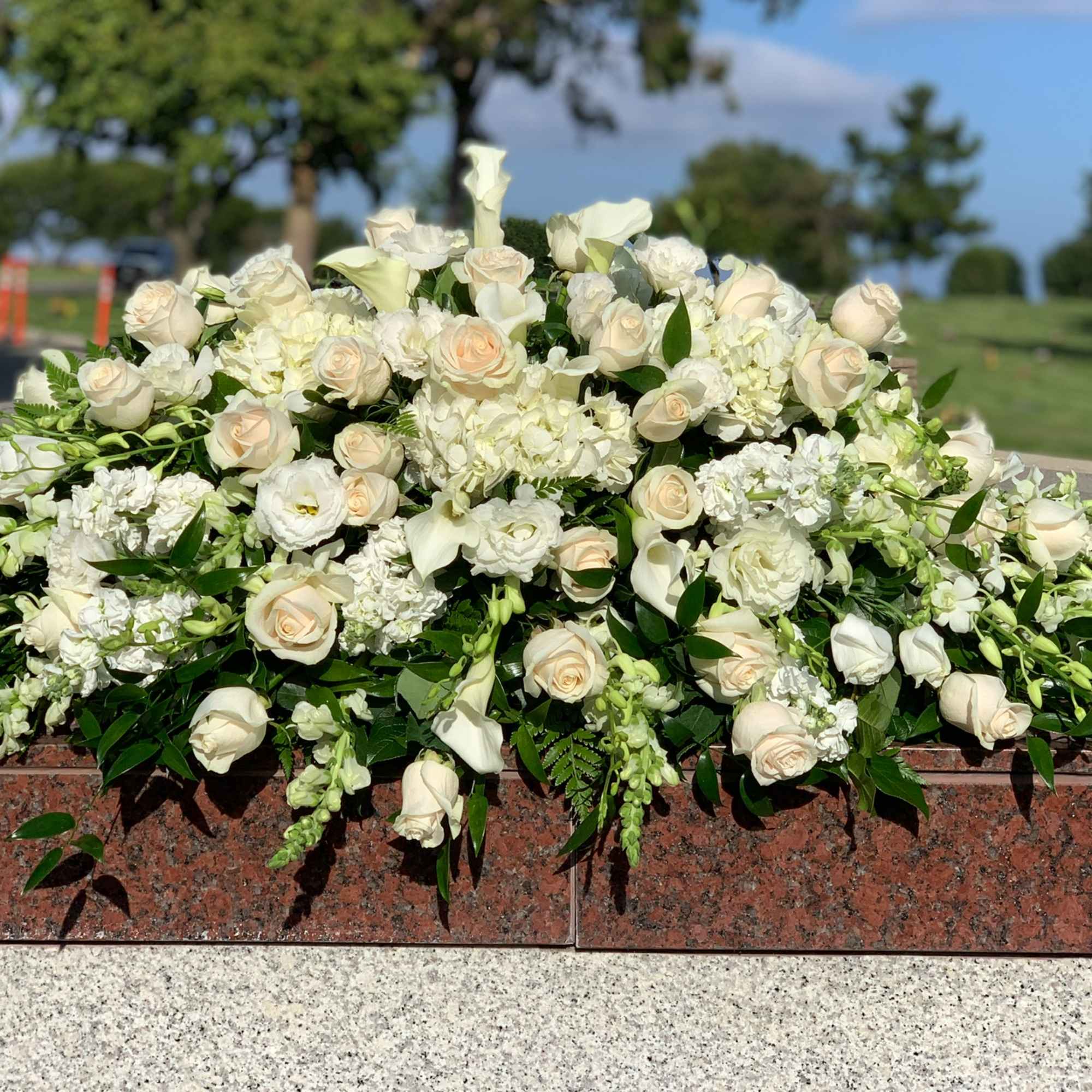 Large white floral arrangement with roses and lilies on a stone memorial