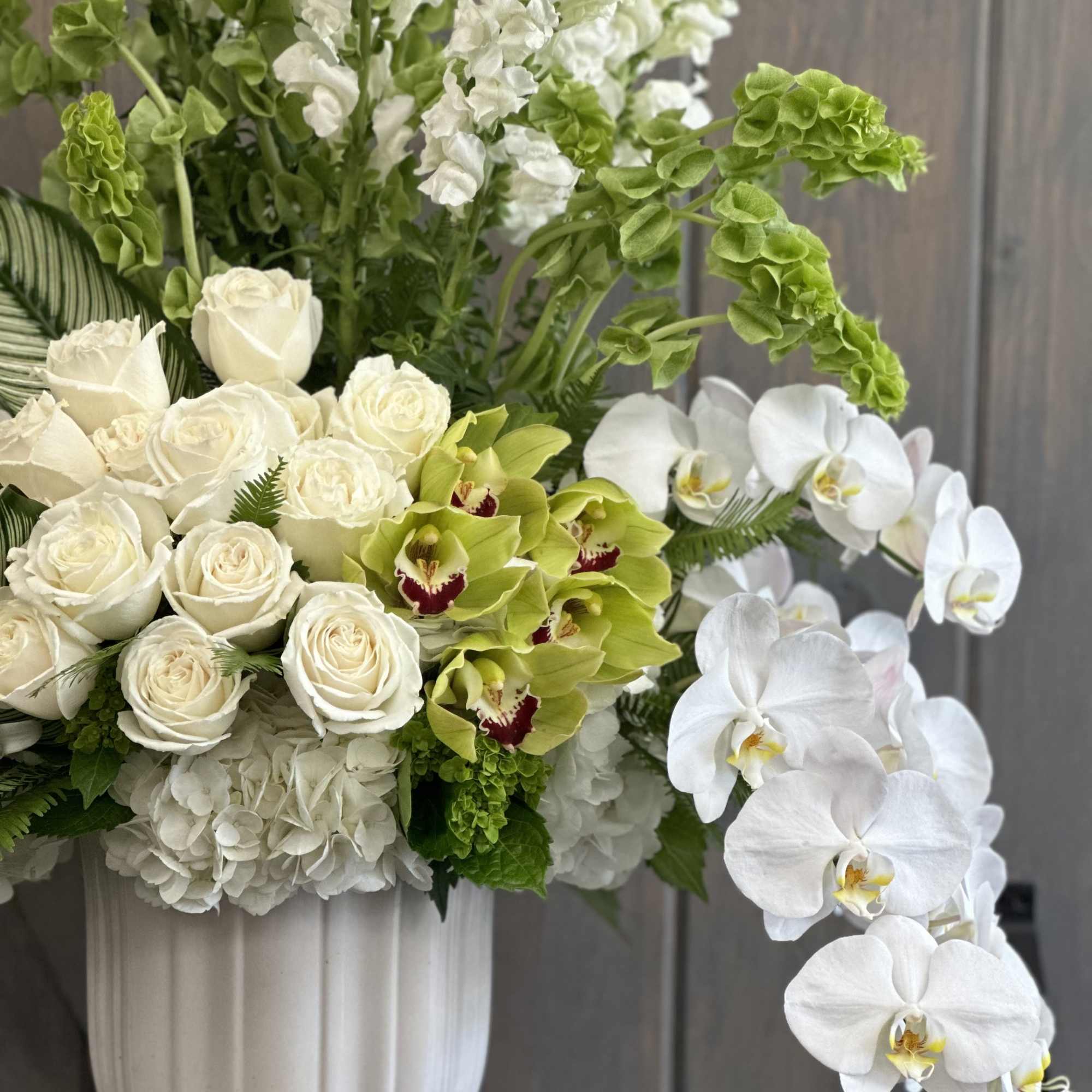 White roses and orchids in a tall white vase