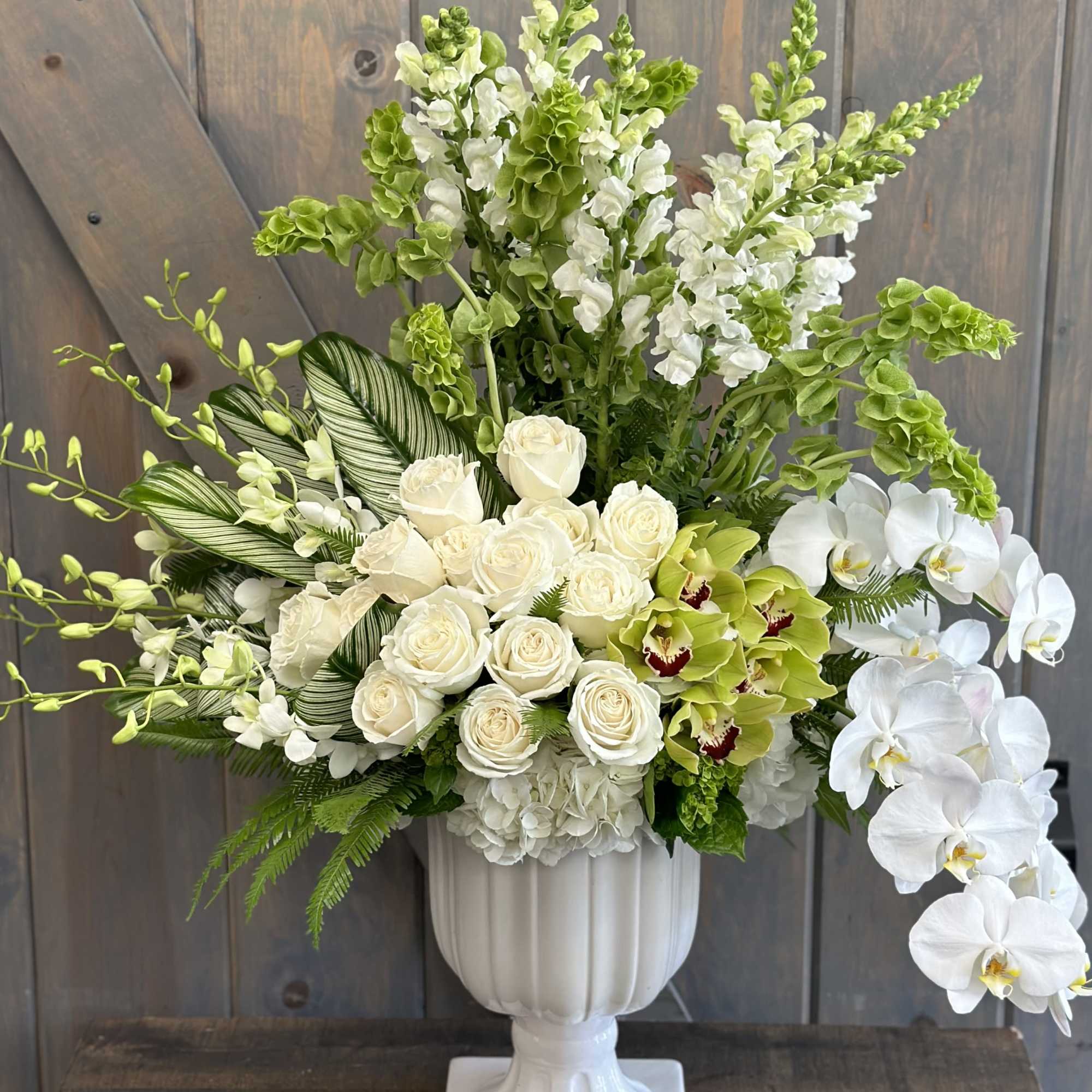 White roses and orchids arranged in a white pedestal vase