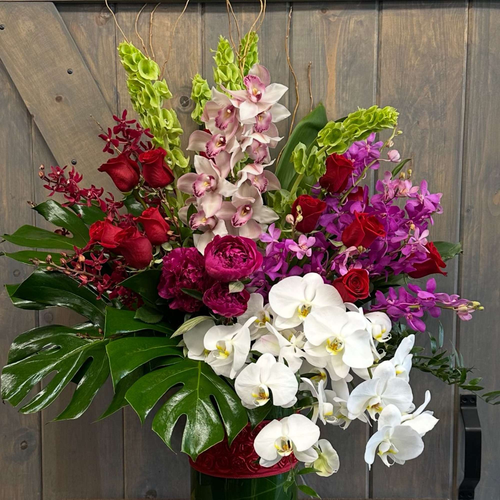 Large tropical arrangement with orchids, roses, and broad leaves in a green vase