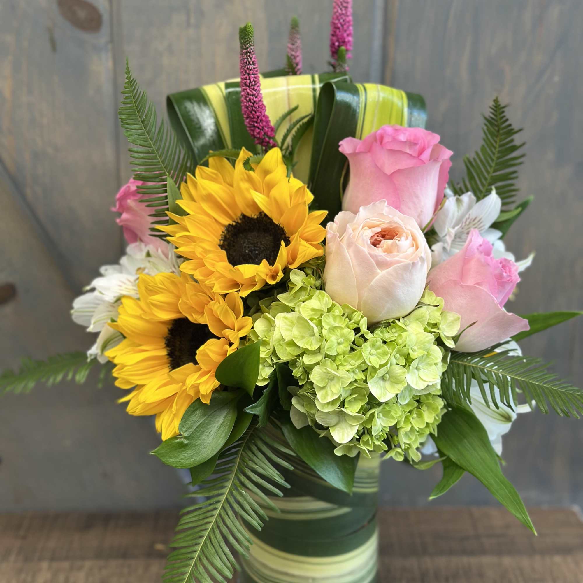Bouquet of sunflowers, pink roses, and green hydrangea in a striped vase