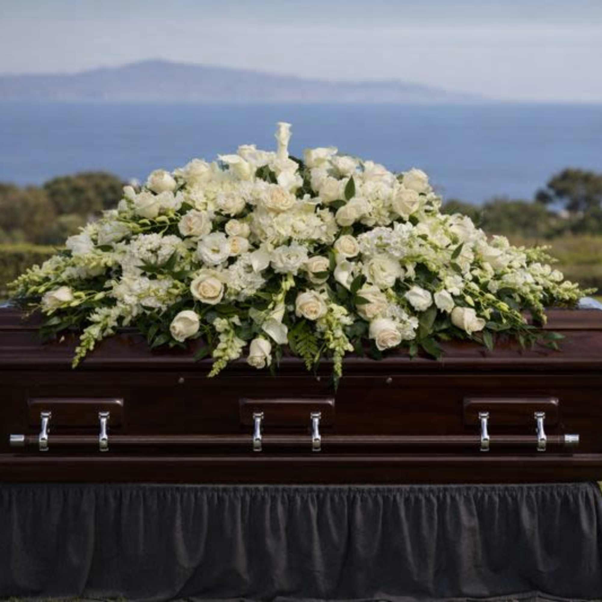 White floral casket spray on a dark wood coffin outdoors