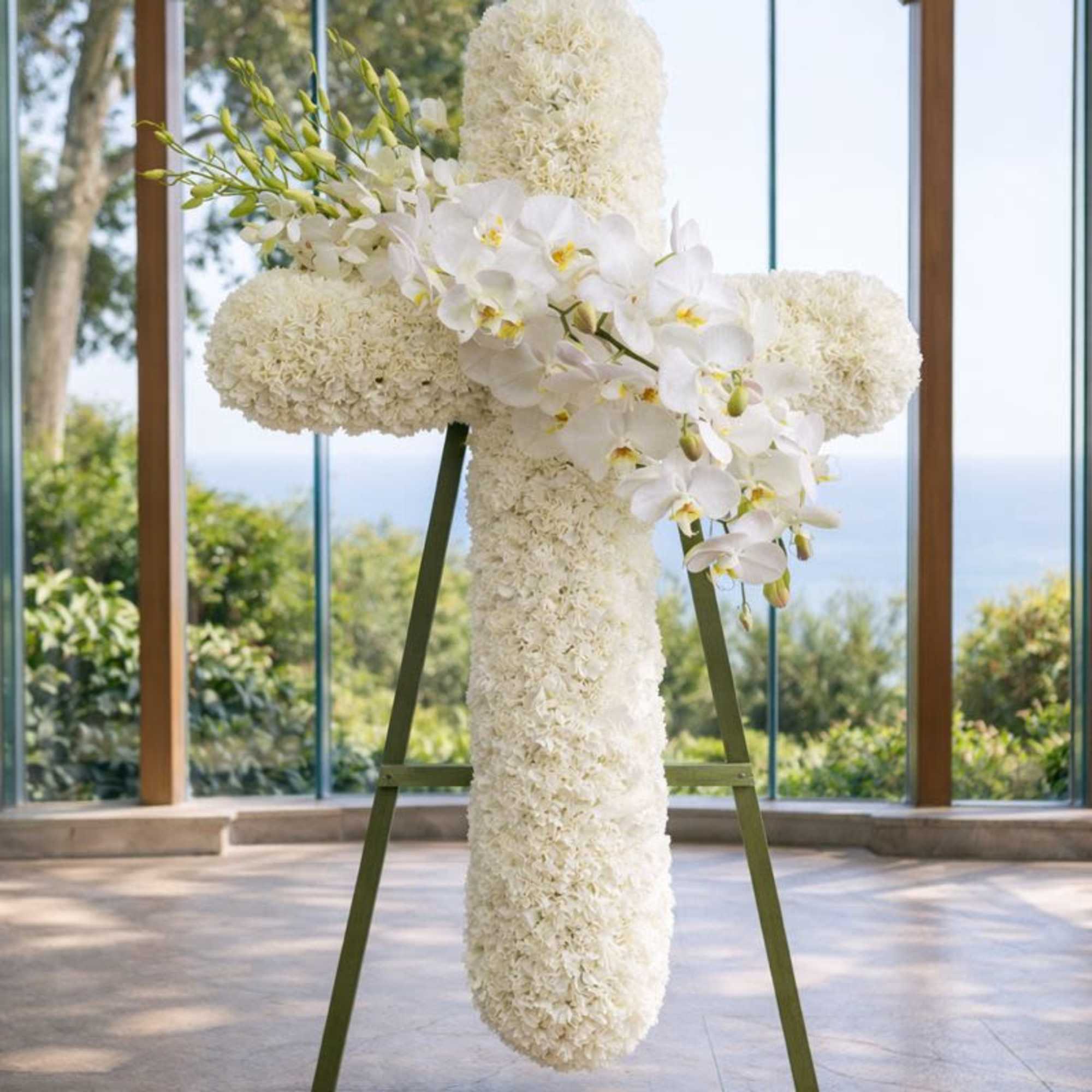 White floral cross on an easel with orchids and clustered blooms