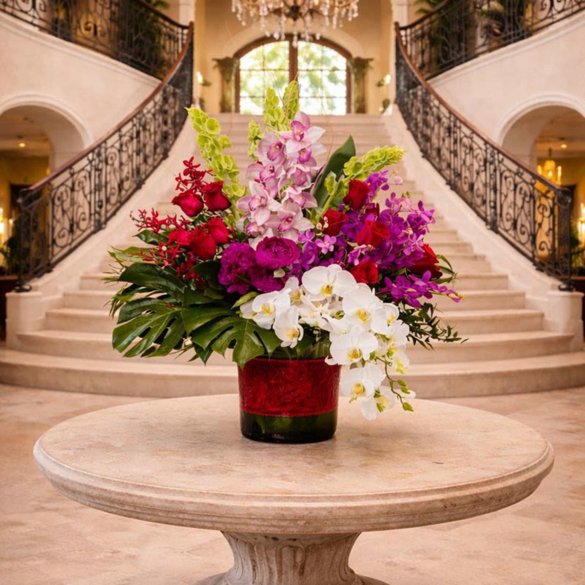 Large mixed orchid arrangement in a red vase on a round table