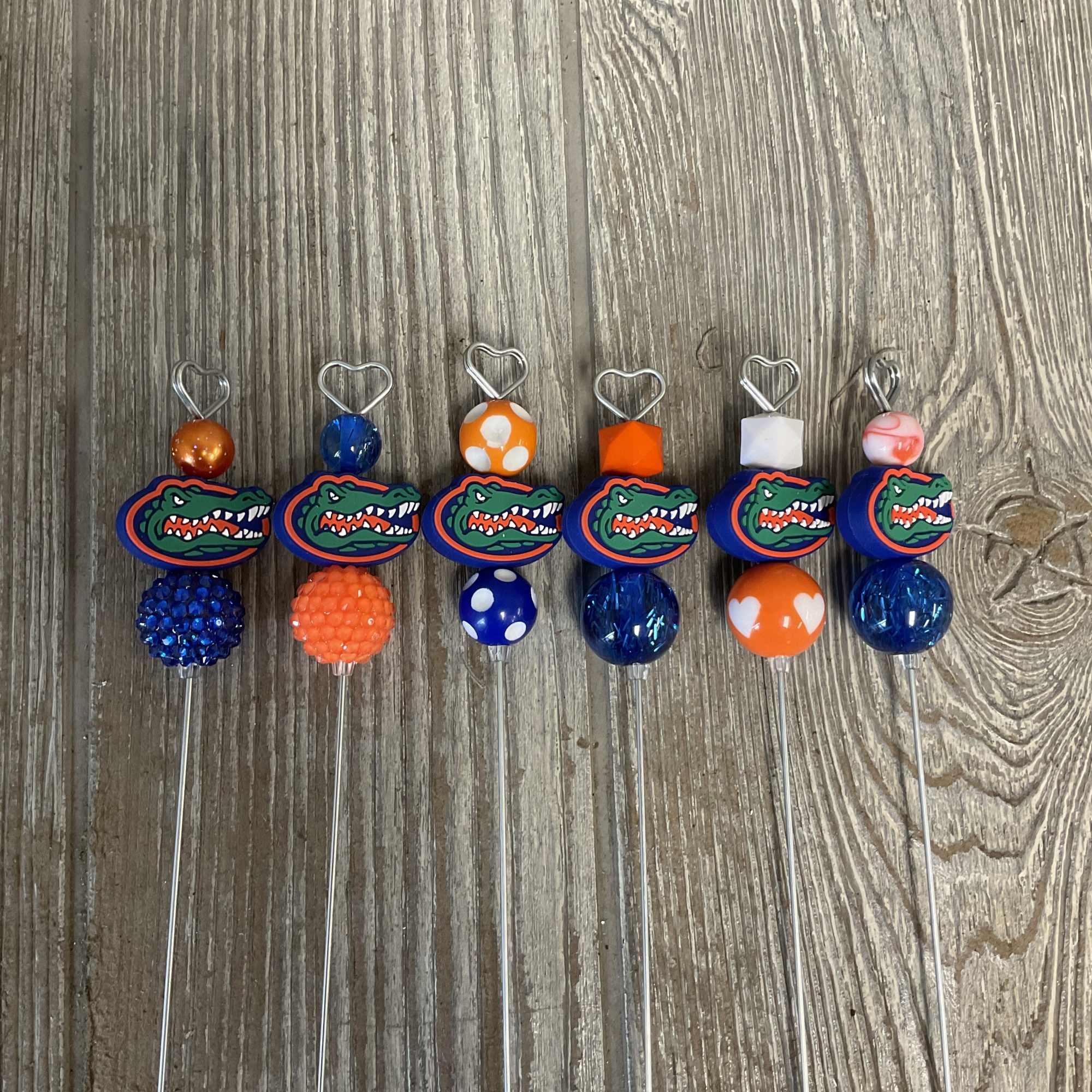 Six Florida Gators bead and charm picks laid on a wood surface.