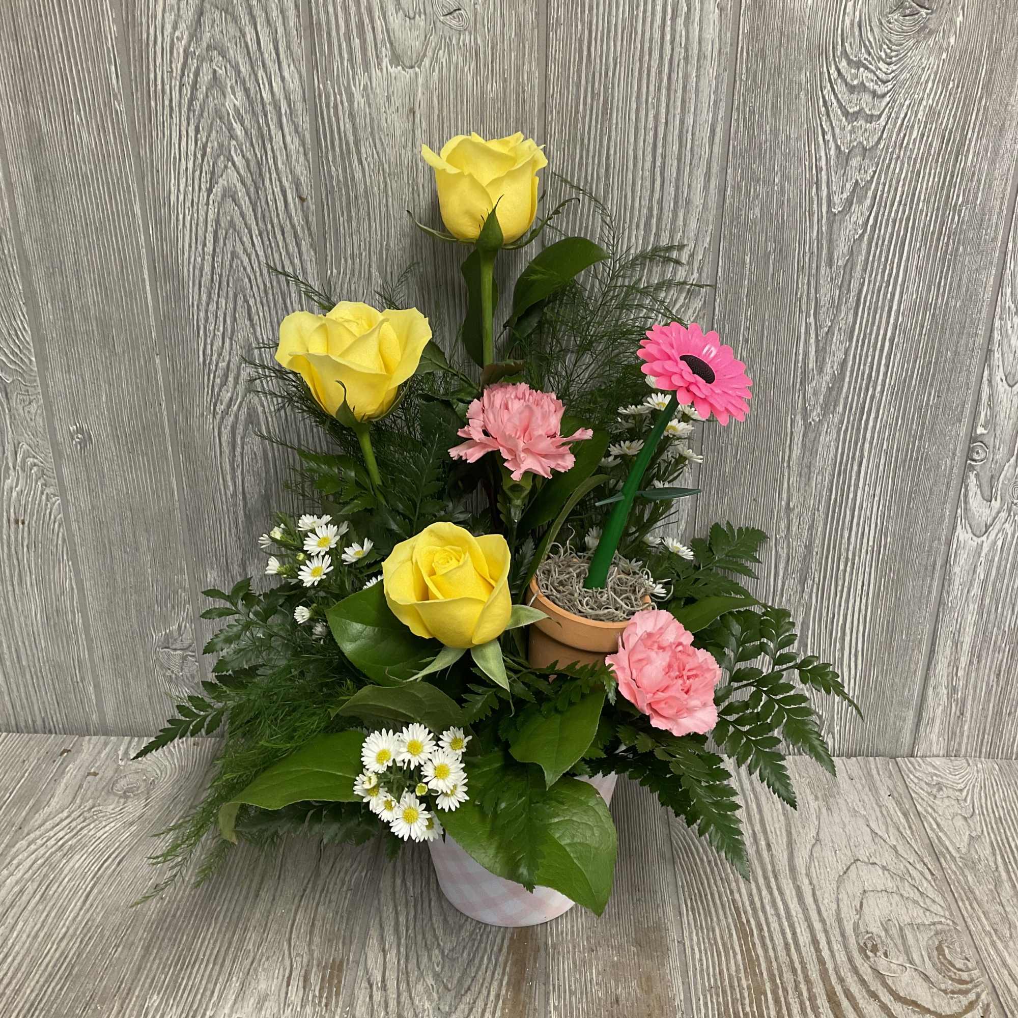Bright roses lift above soft carnations and cheerful daisy-style blooms in this