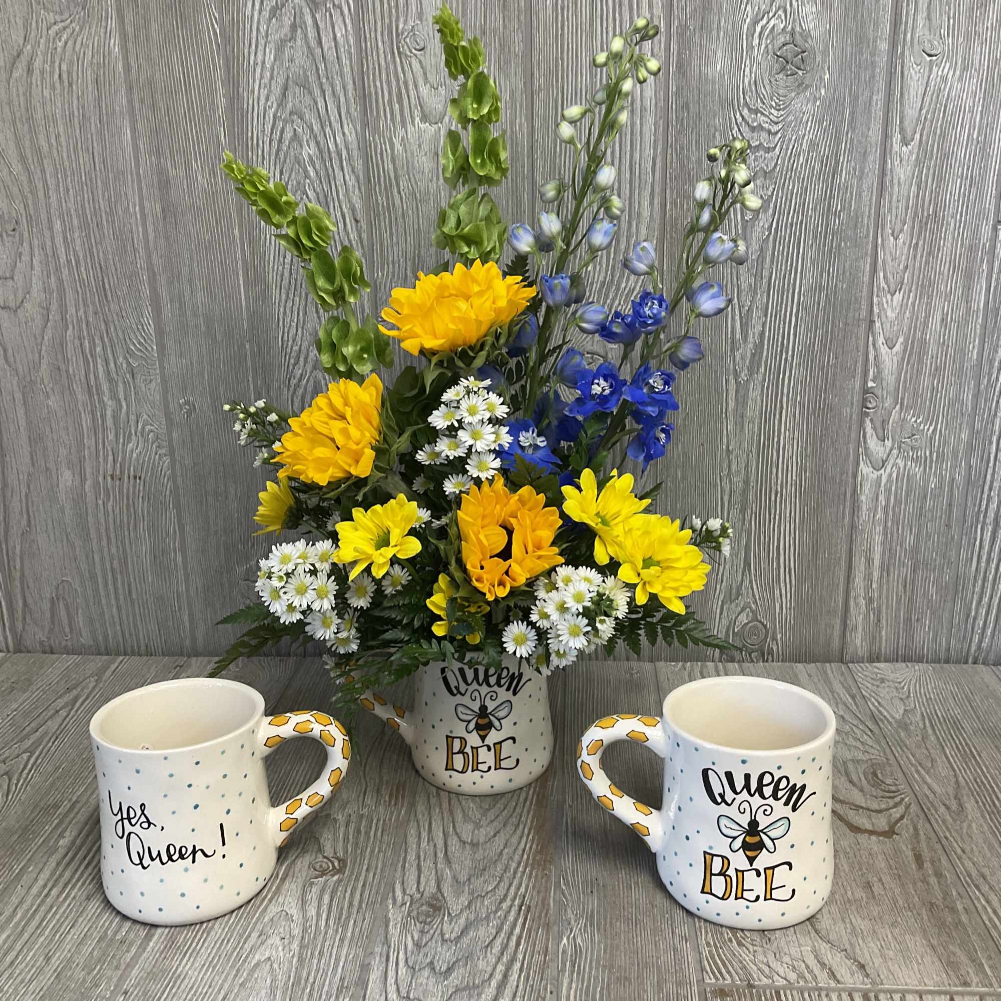 Yellow and blue flower arrangement in a bee-themed mug, flanked by two matching mugs