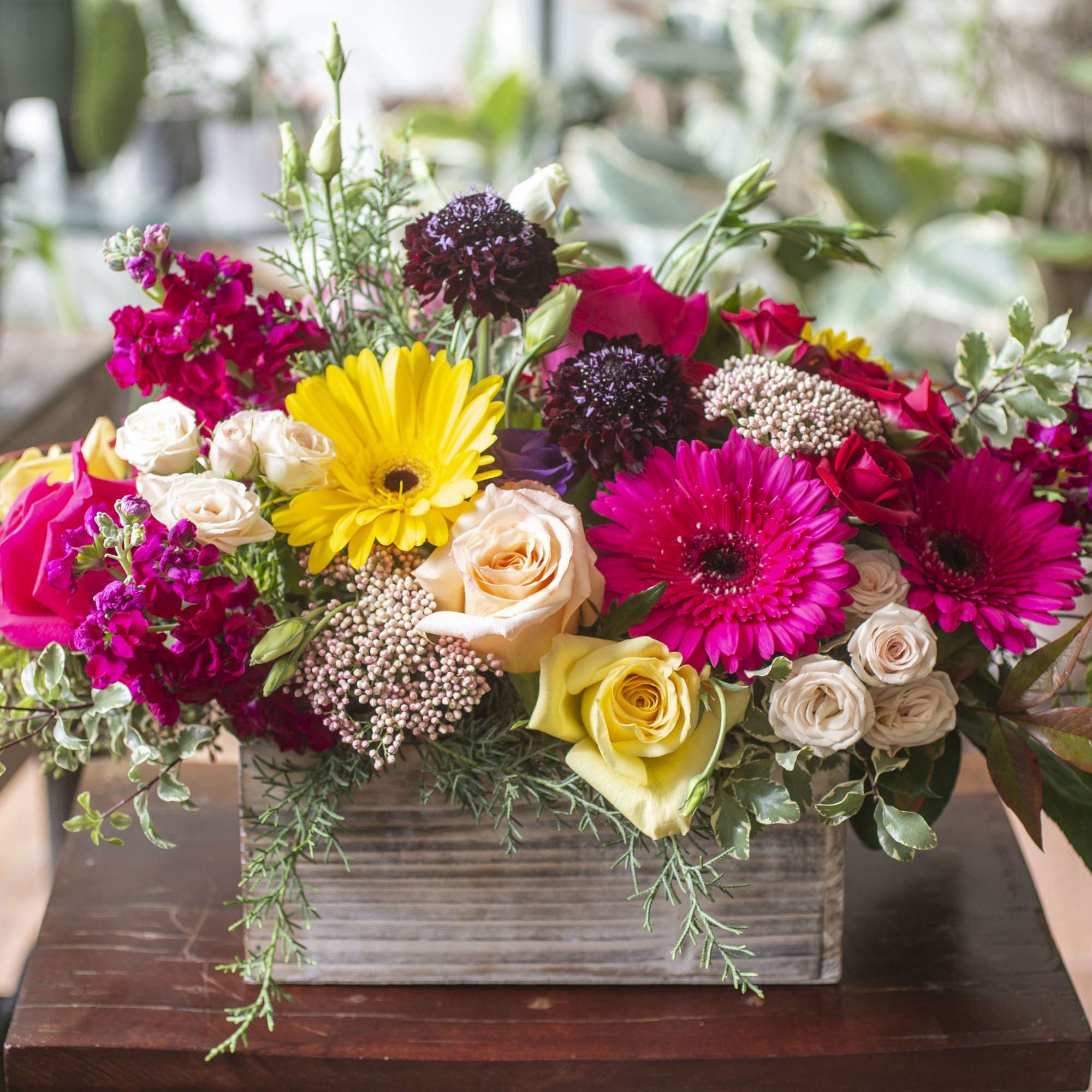 Bright mixed flower arrangement in a wooden box with roses and gerbera daisies