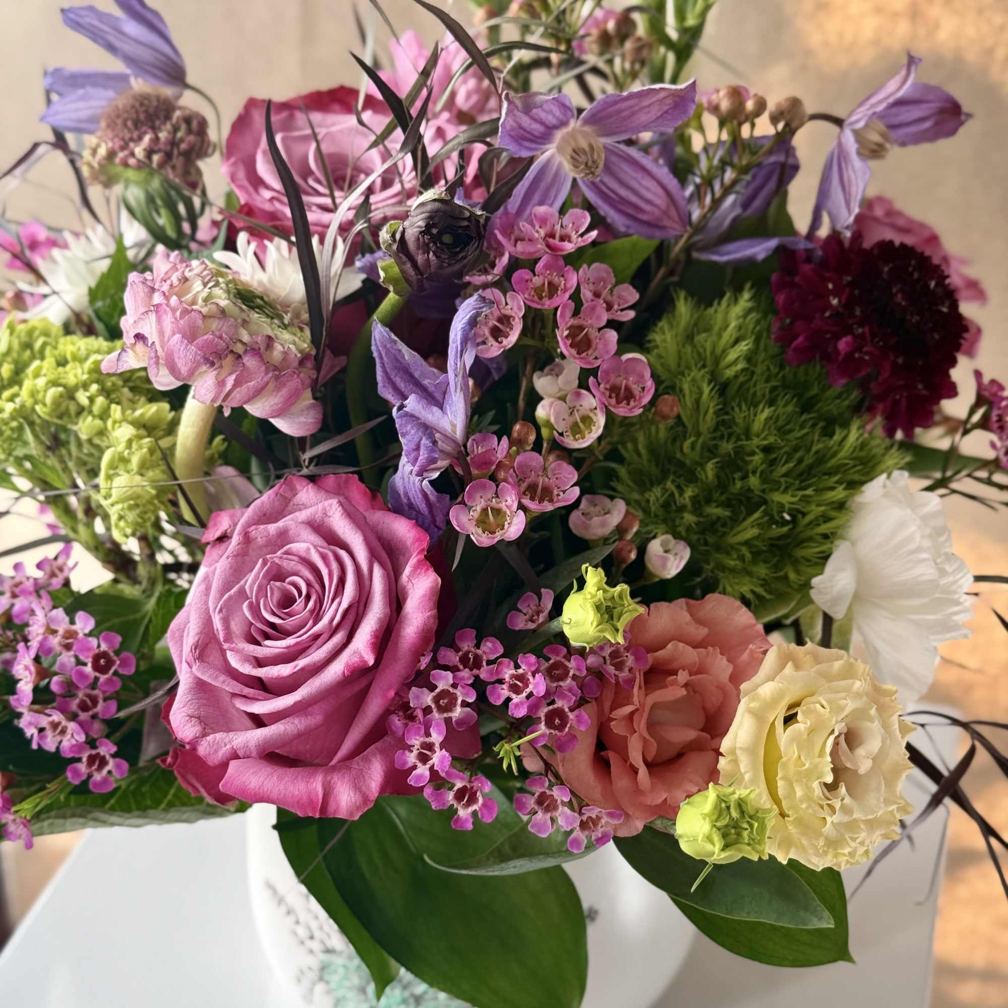 Mixed bouquet of pink, purple, and cream flowers in a white vase