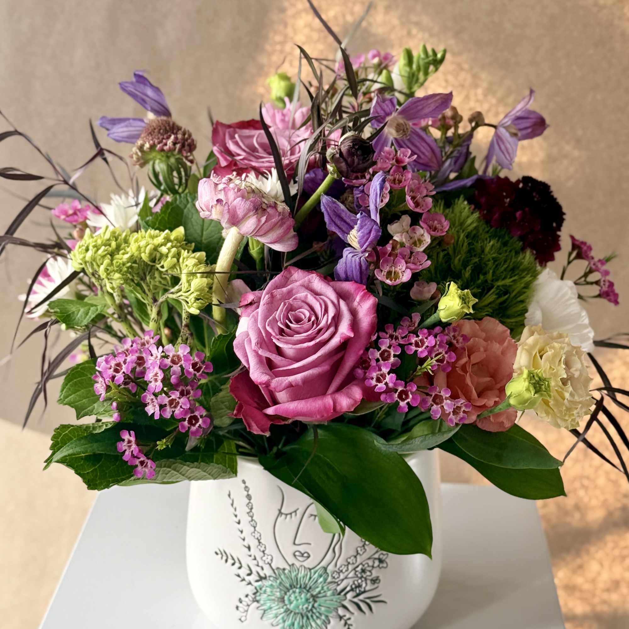 Mixed bouquet of pink, purple, and white flowers in a white vase