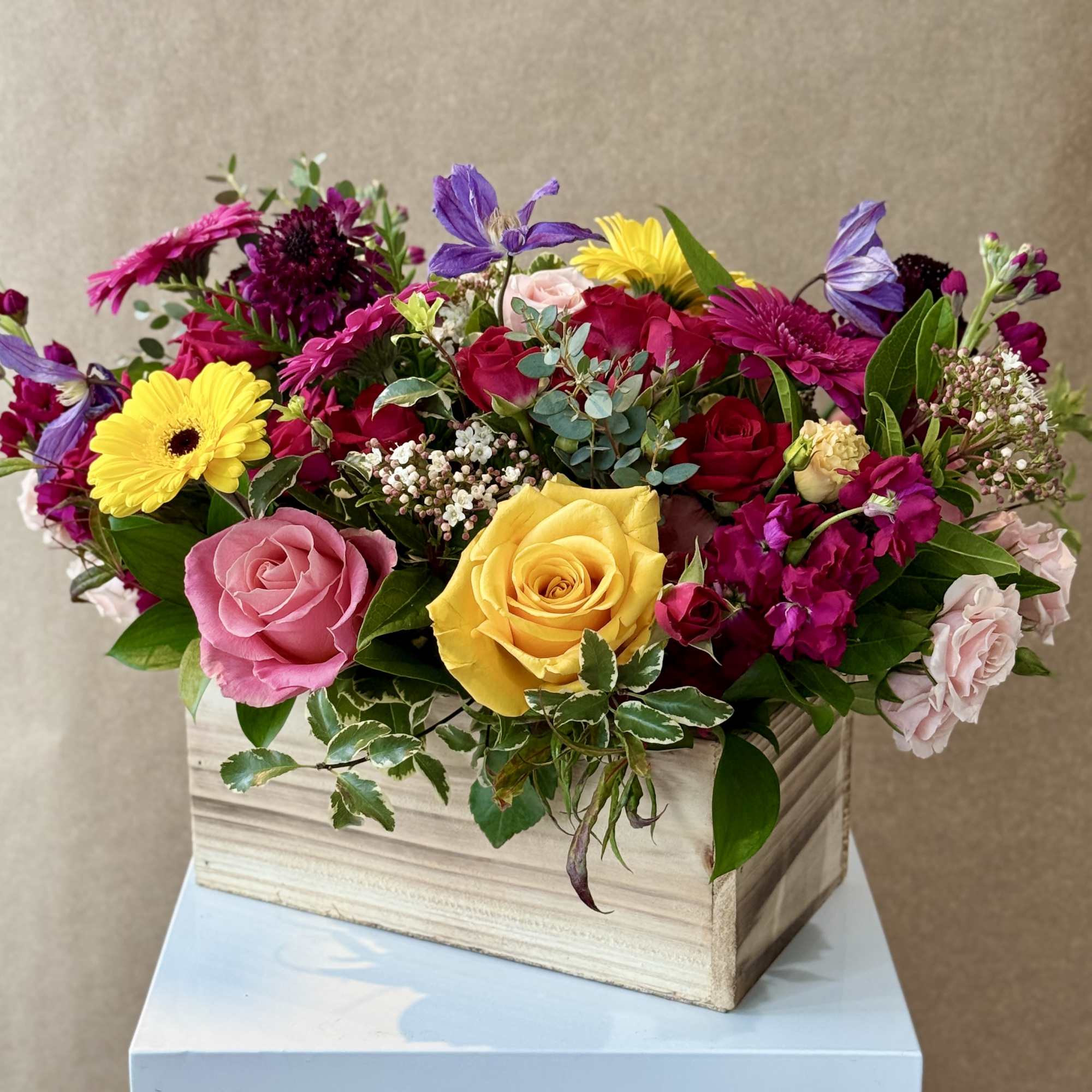 Mixed bouquet of roses, gerbera daisies, and purple blooms in a wooden box