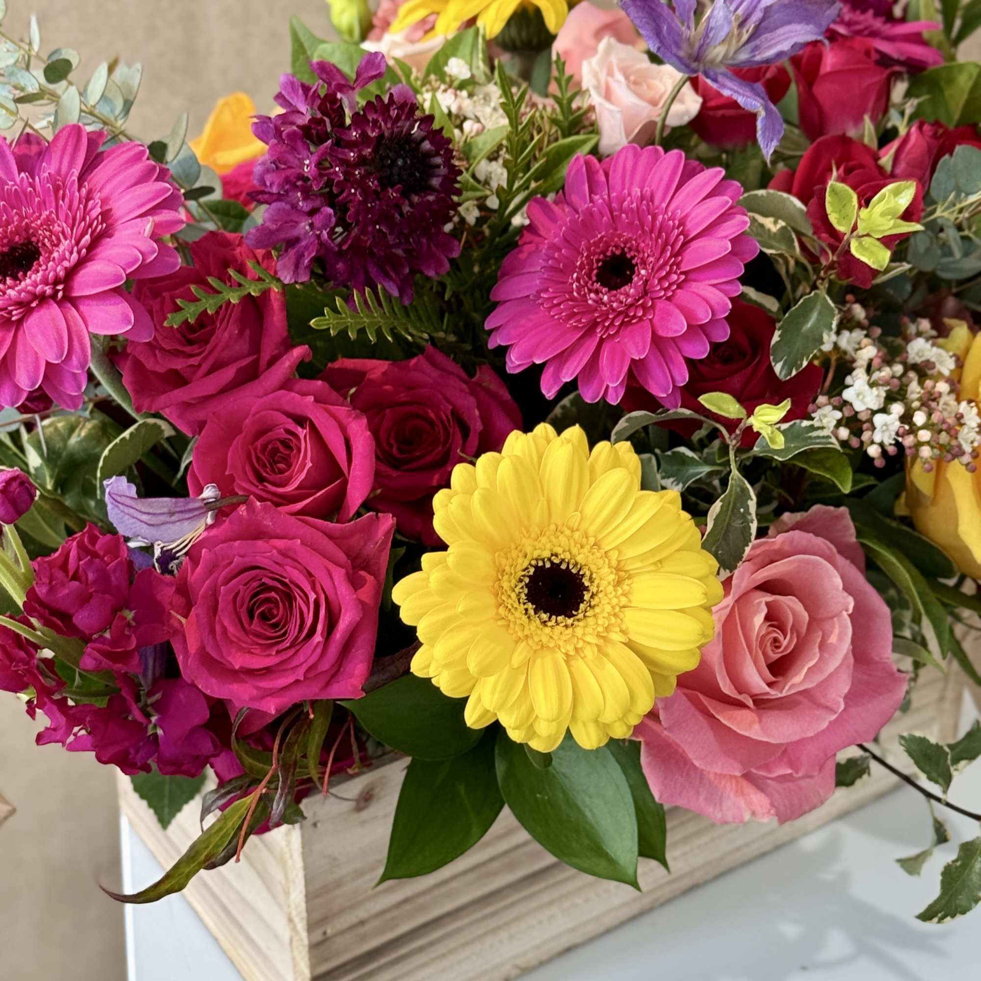 Mixed bouquet of pink roses, yellow and pink gerbera daisies, and purple blooms in a wooden box