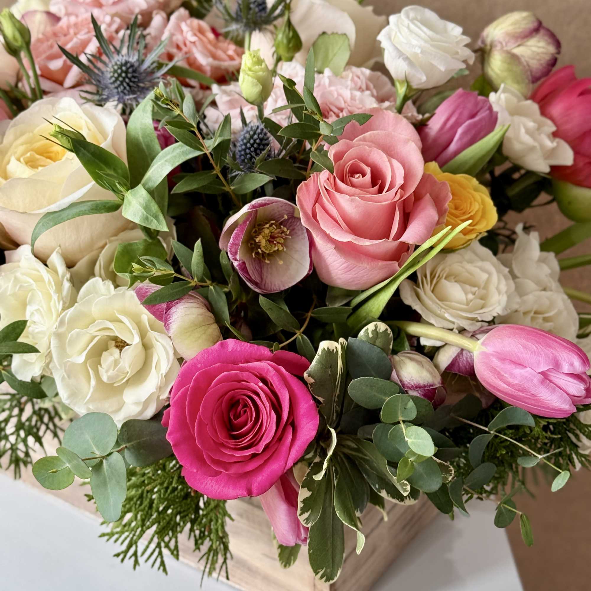 Mixed bouquet of roses, tulips, and hellebores in a wooden box