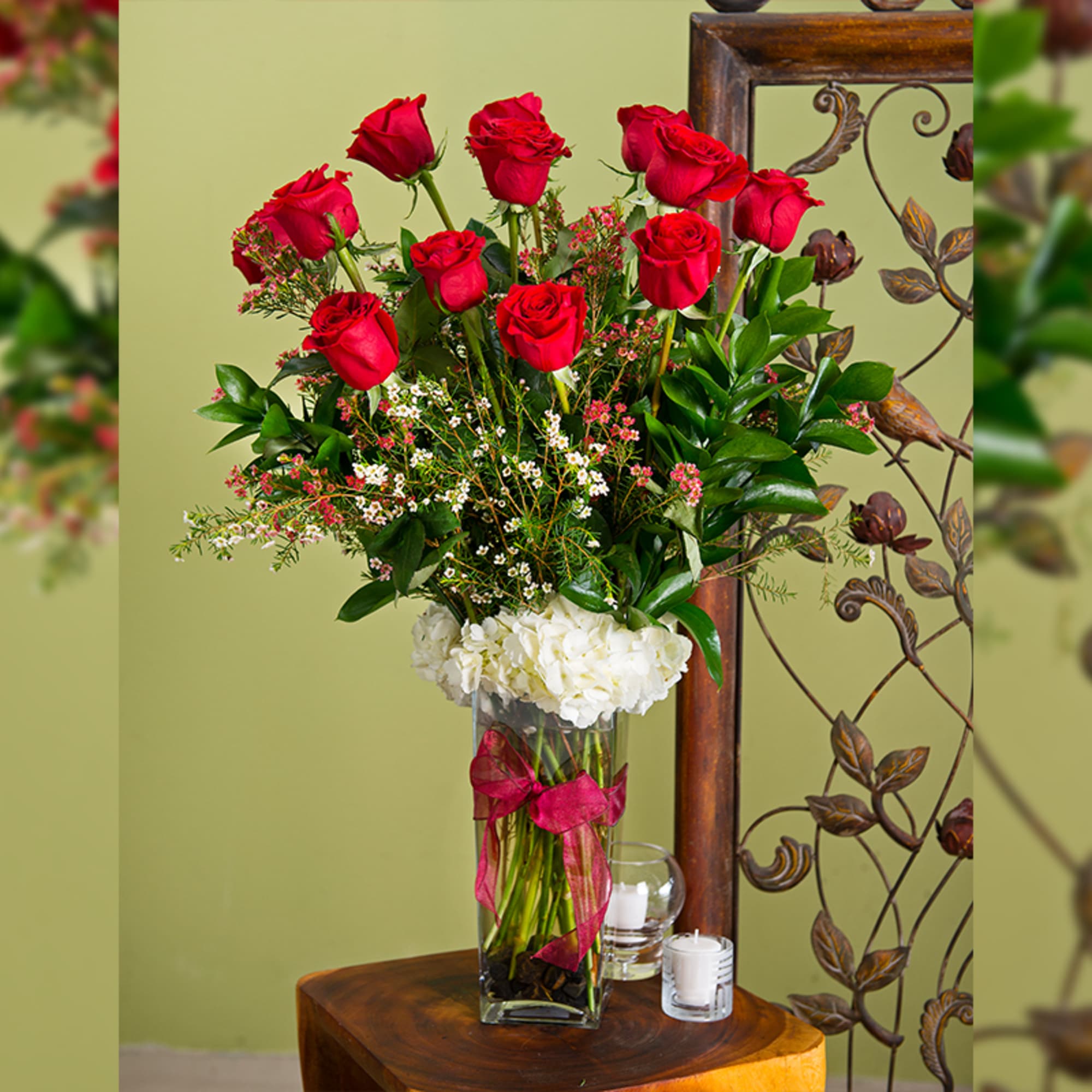 Tall vase arrangement of red roses with white hydrangea and a pink ribbon