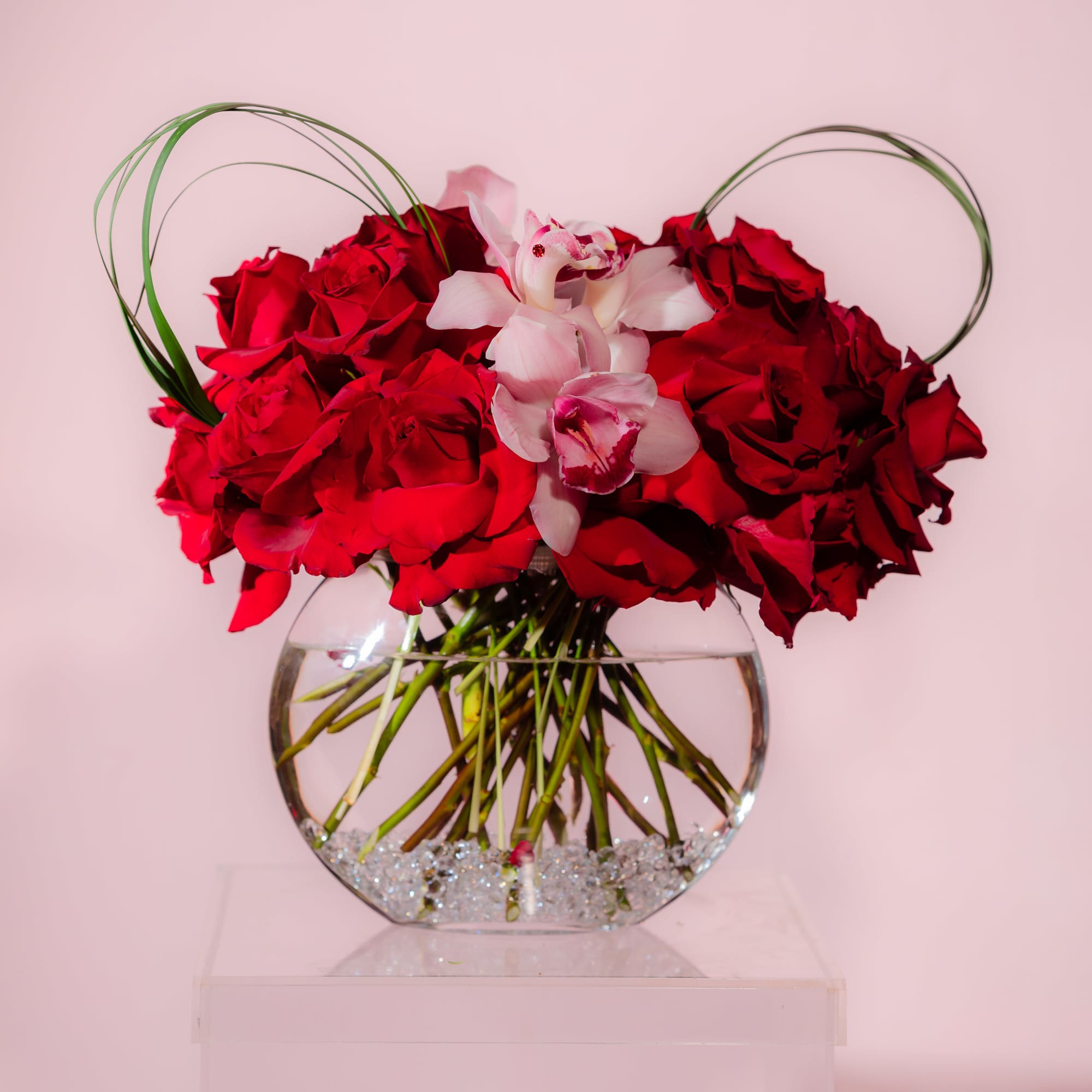 Red rose arrangement with pink orchids in a round glass vase