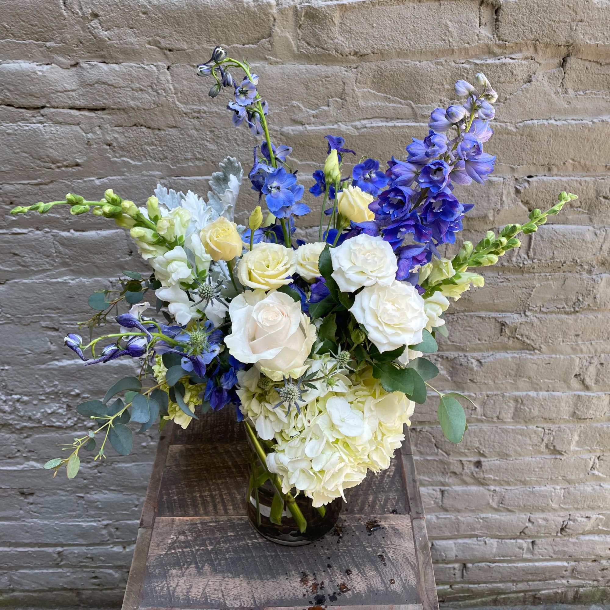 Tall arrangement of white roses, hydrangeas, and blue delphinium in a clear glass vase