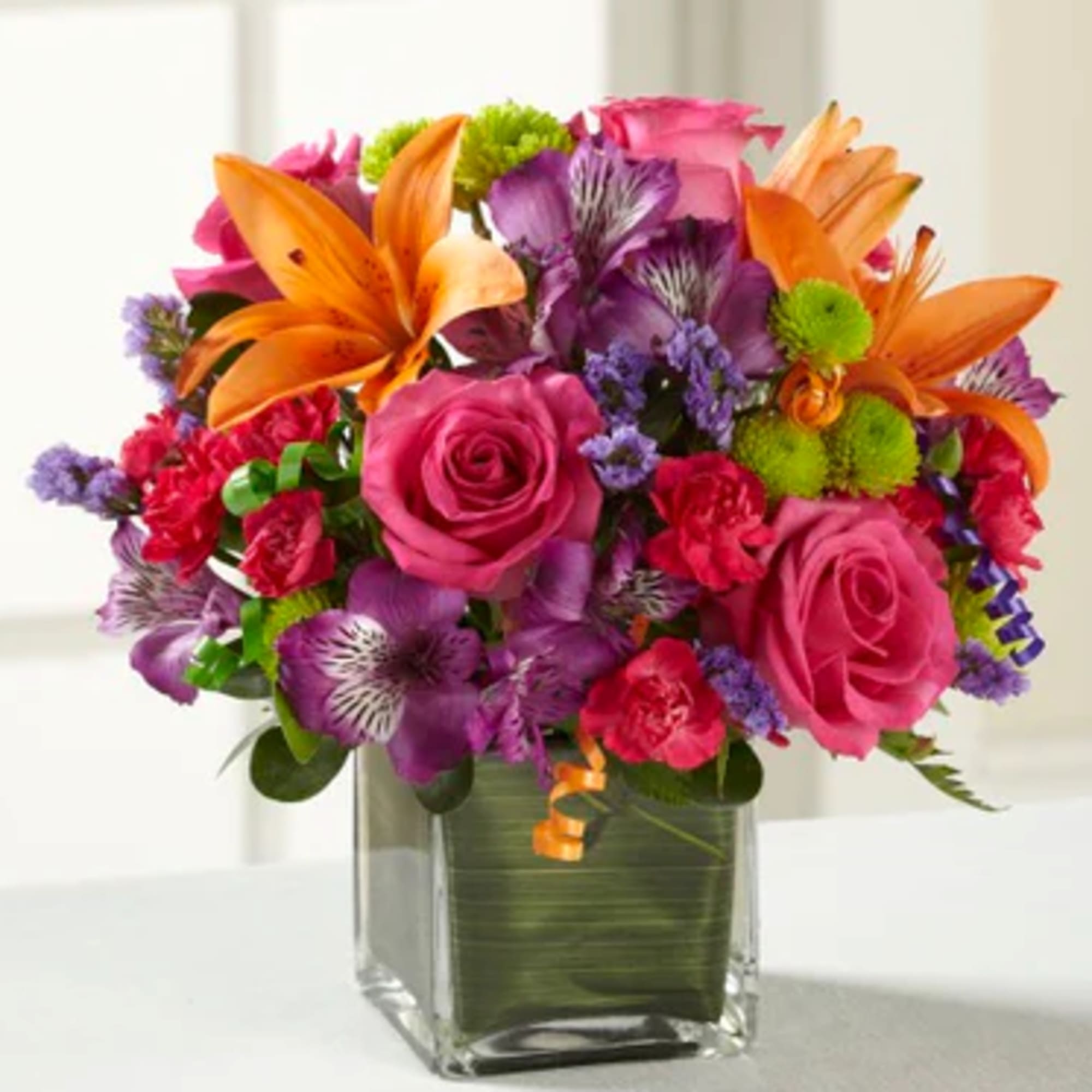 Bright mixed bouquet with pink roses, purple flowers, and orange lilies in a glass vase