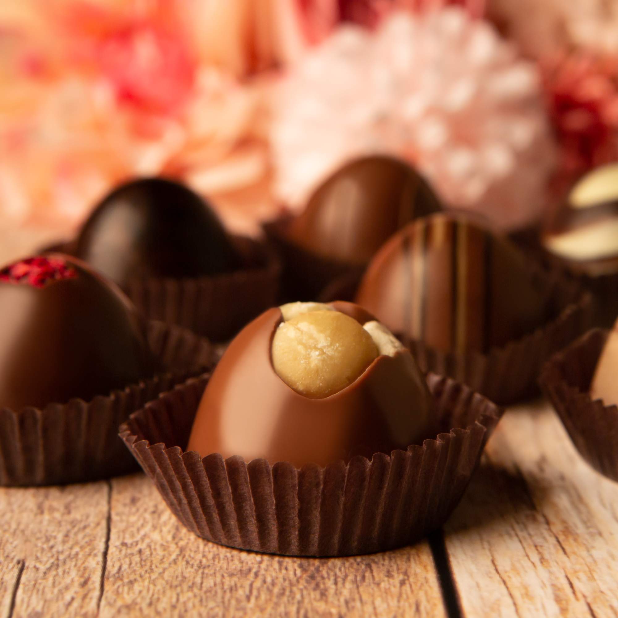 Assorted round chocolate truffles in brown paper cups on a wooden surface.