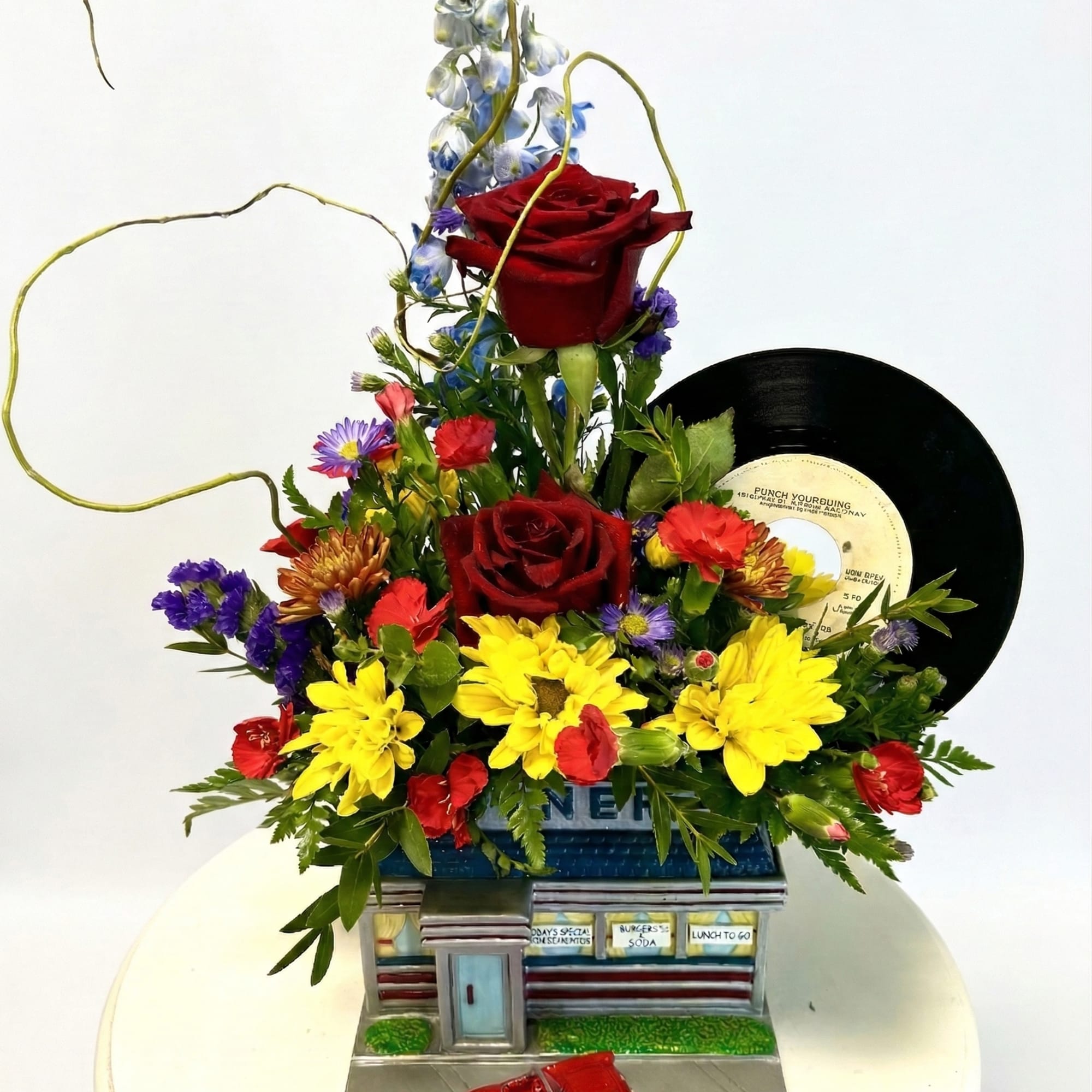 Floral arrangement with red roses, yellow daisies, and a vinyl record display