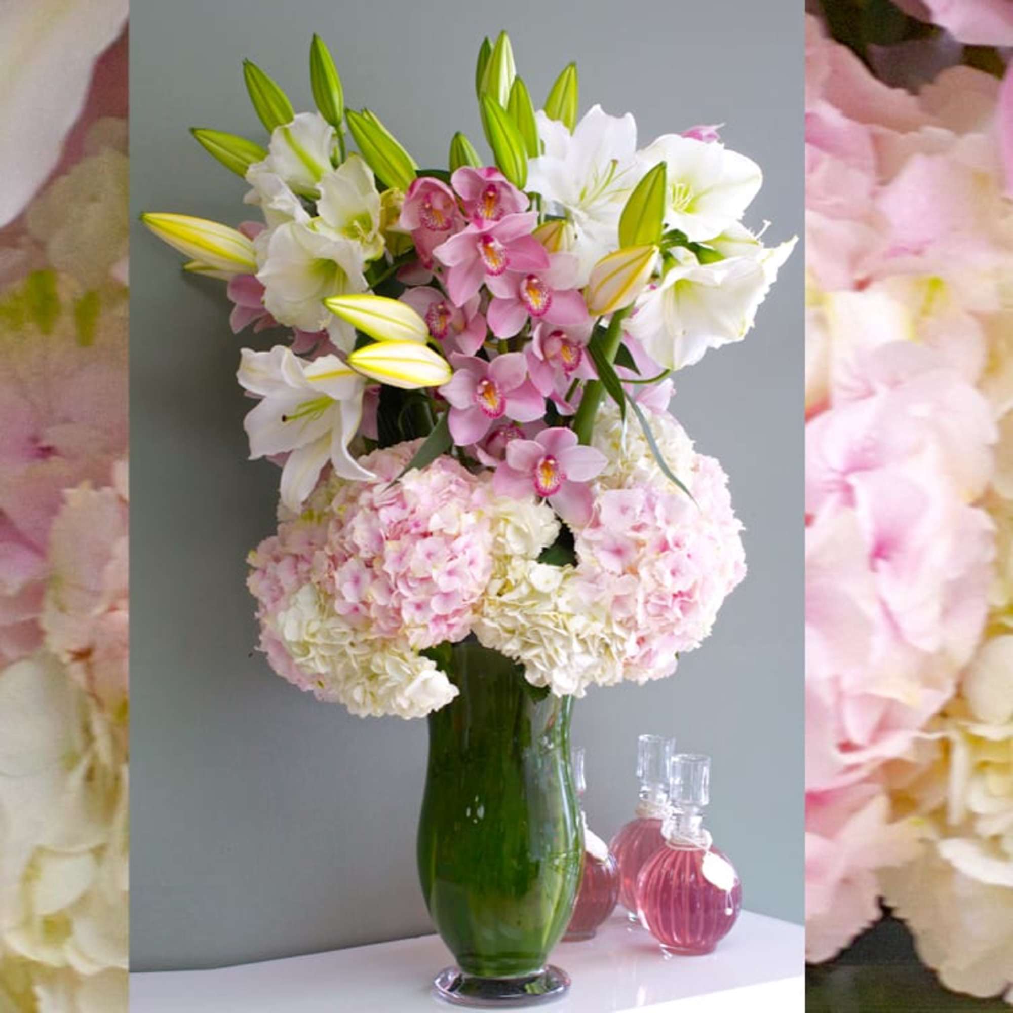 Pink orchids and white lilies in a green glass vase with pale hydrangeas