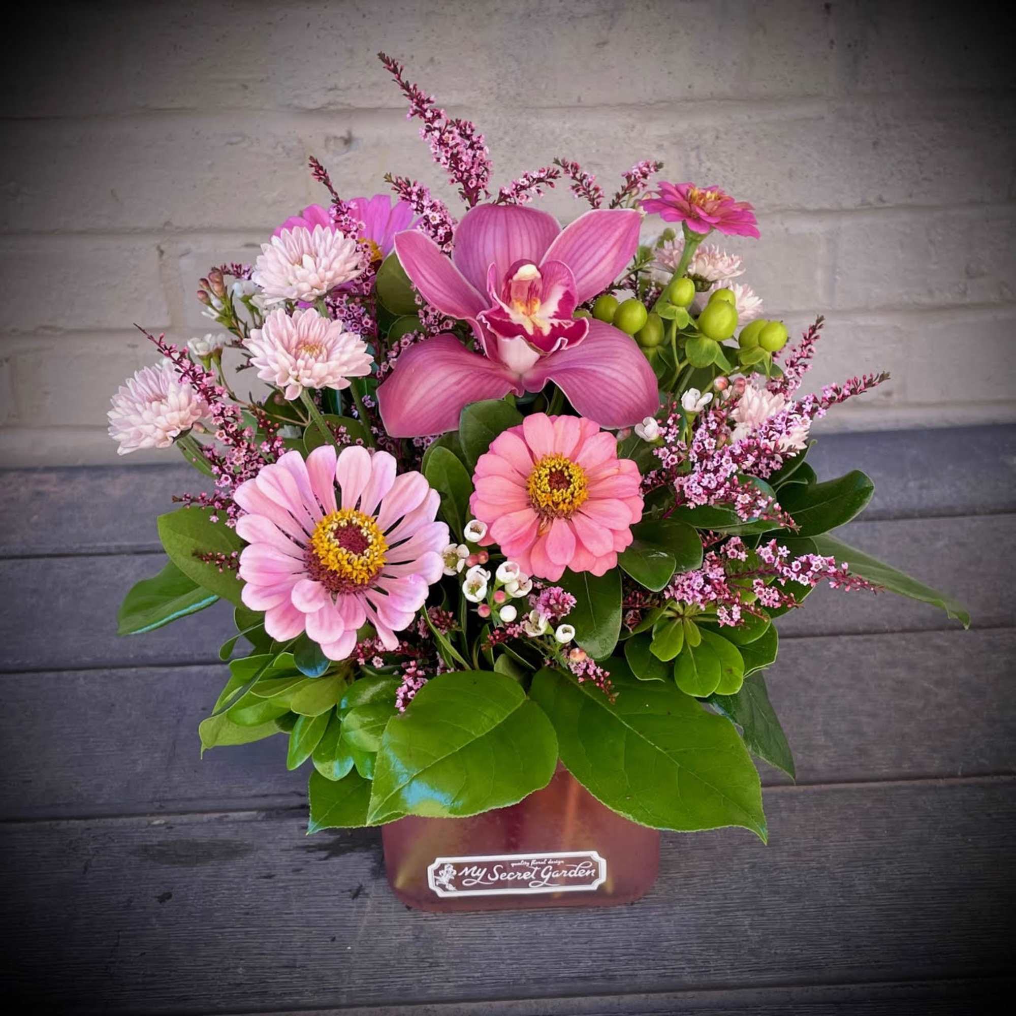 Pink orchid and daisy arrangement in a square container
