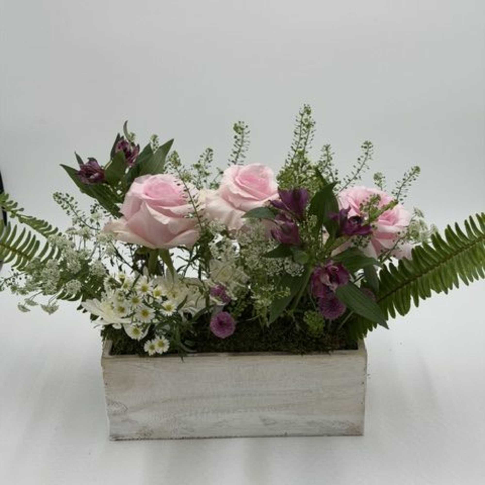 Pink roses and purple flowers arranged in a rectangular wooden box